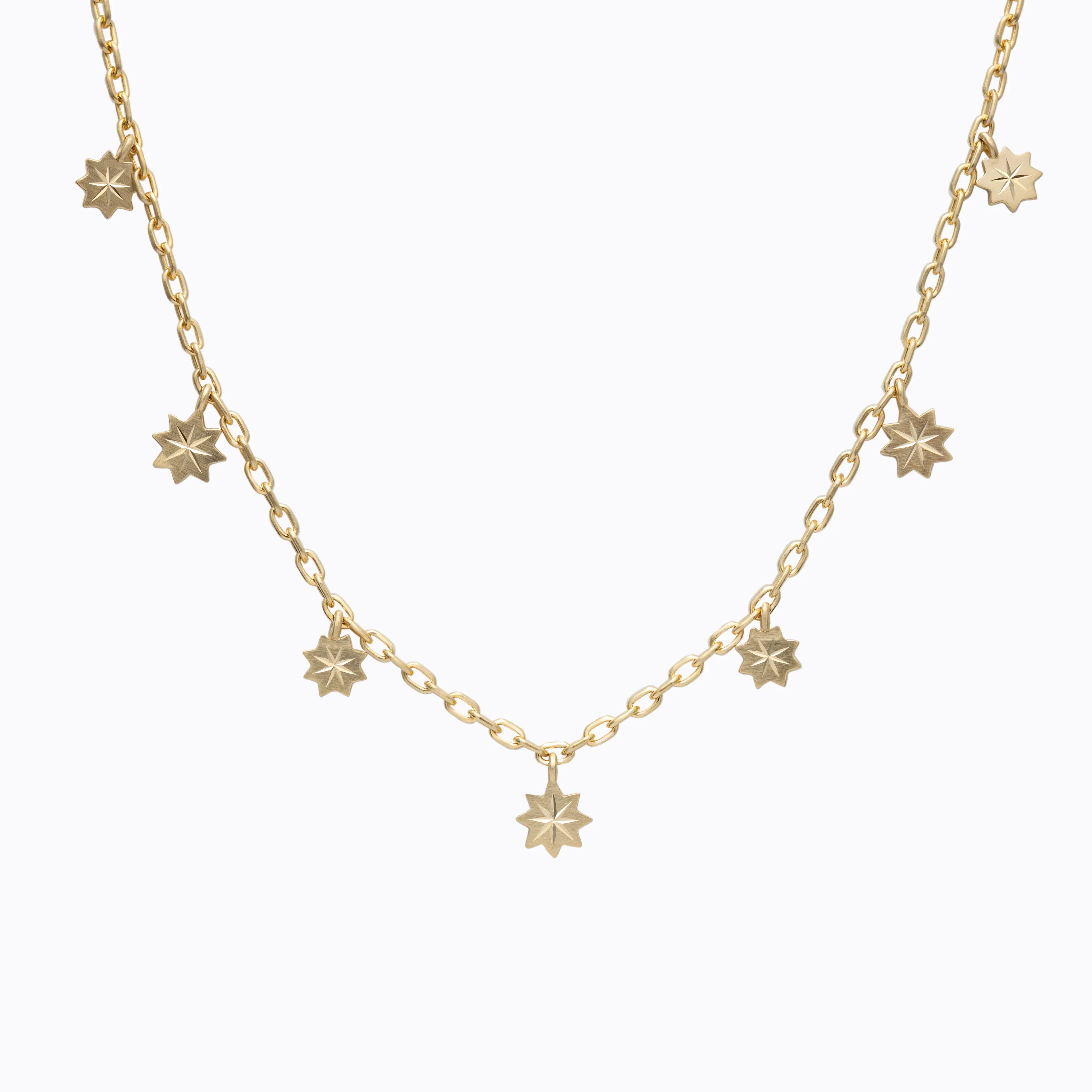 Elegant gold chain necklace with seven small engraved star charms on soft white background
