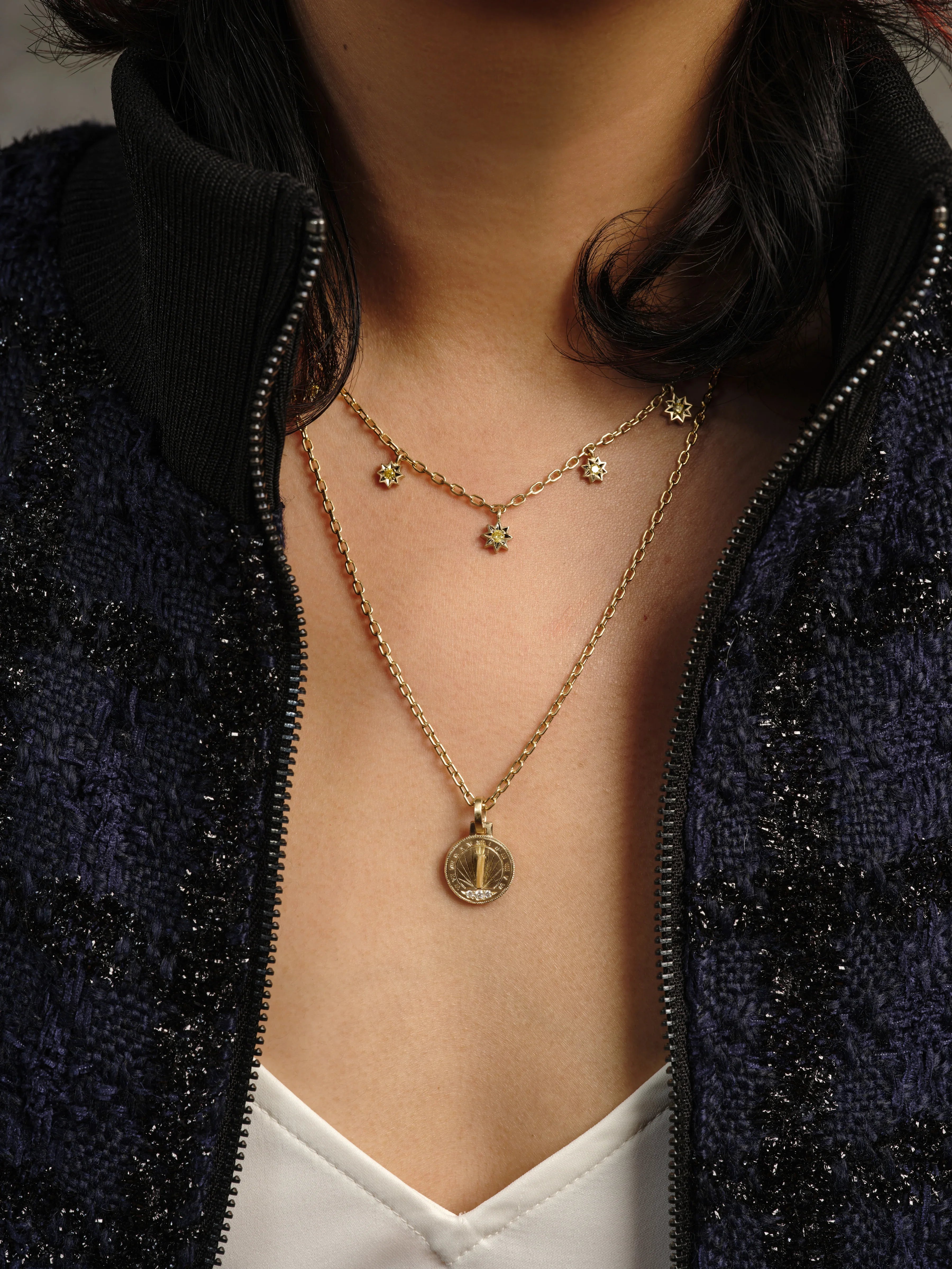 Close-up of woman wearing layered Fairmined gold necklaces, sundial pendant and star charms, soft warm light