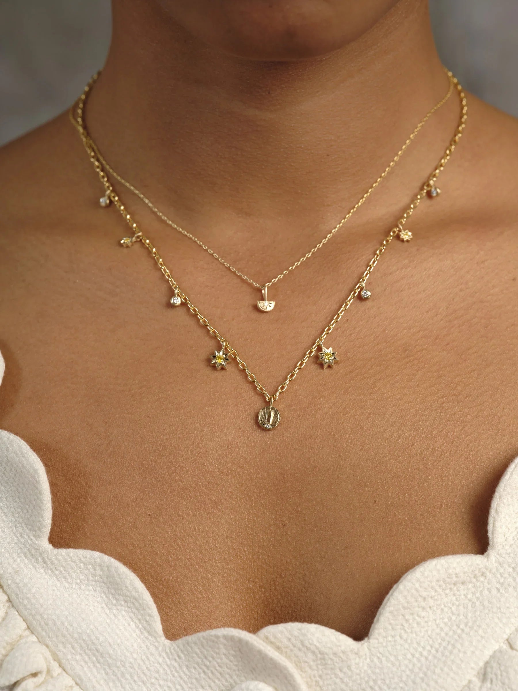 Close-up of layered Fairmined gold necklaces with star and shell pendants on warm skin, soft natural light