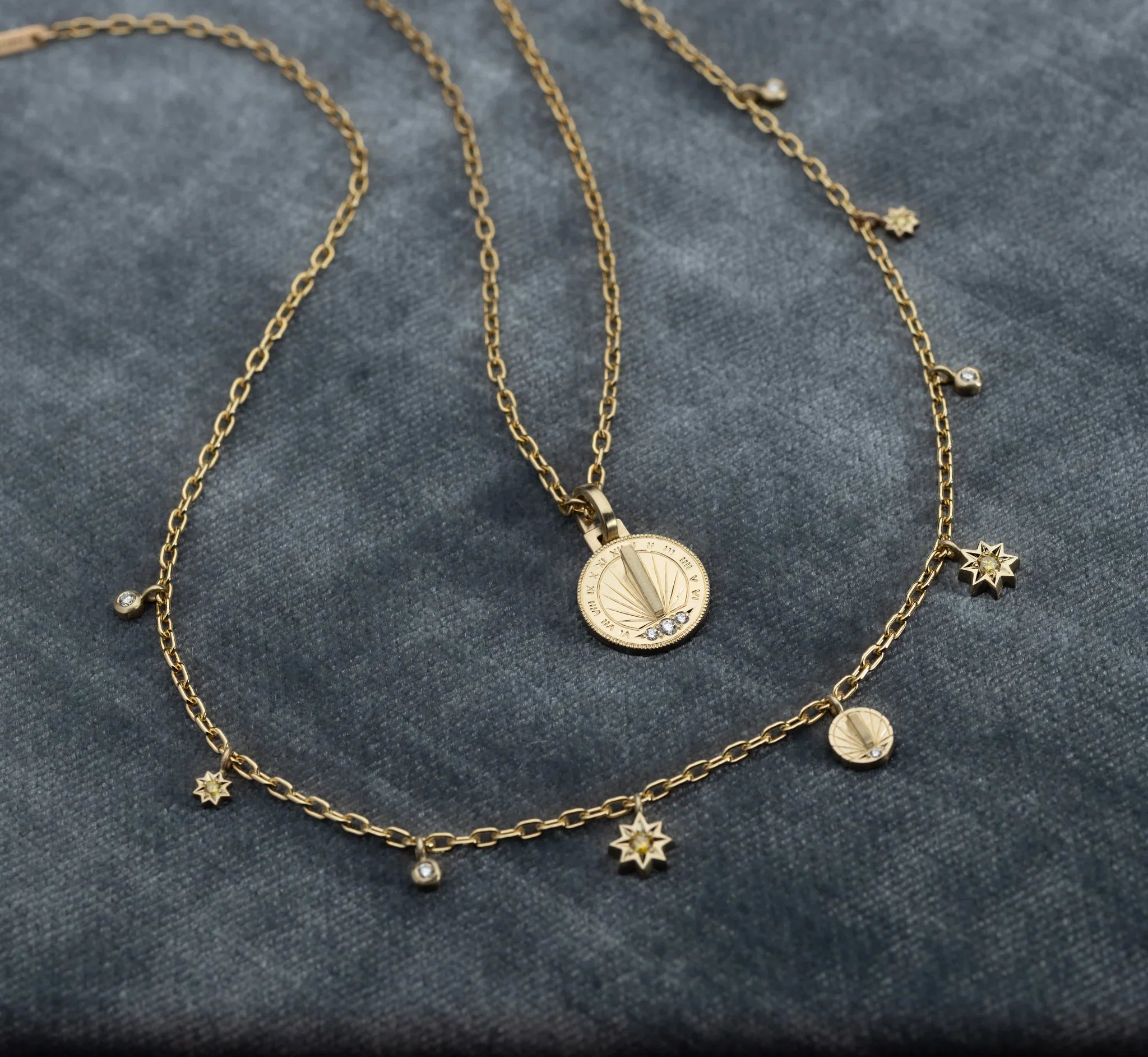 Close-up of delicate gold sundial pendant and star charm necklace on soft grey fabric with warm, natural light