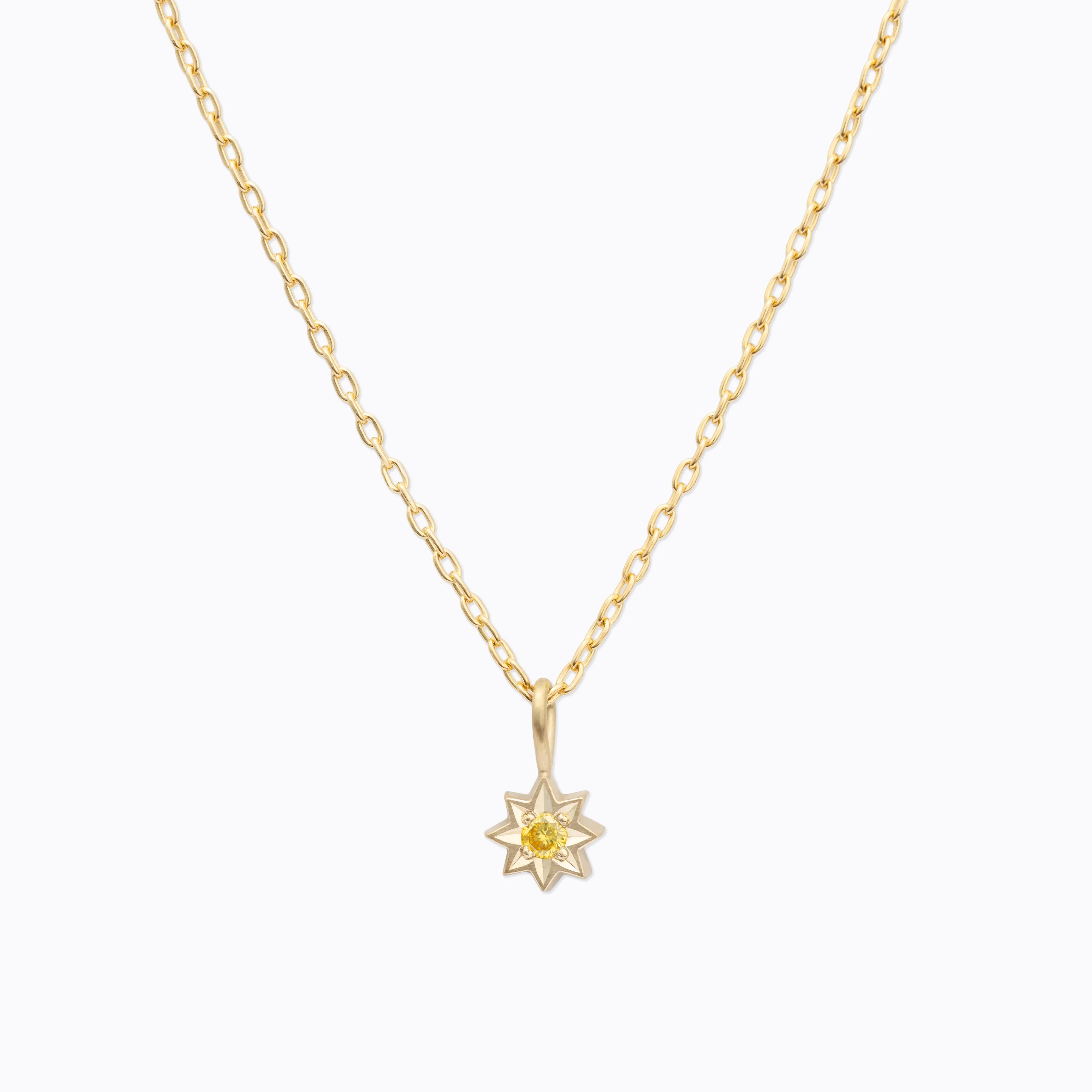 Delicate gold star pendant necklace with central yellow gemstone on clean white background