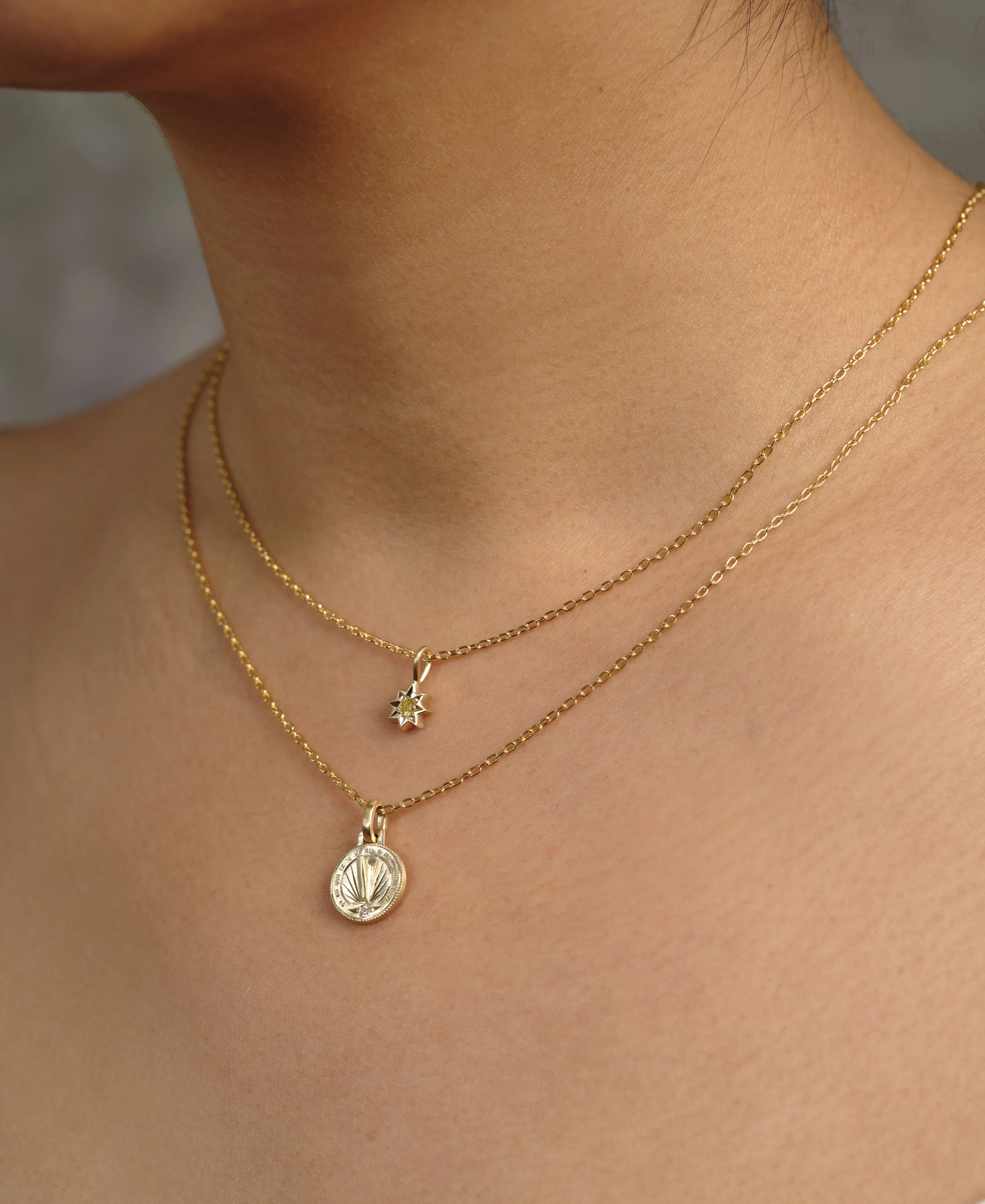 Close-up of layered Fairmined gold necklaces with delicate sun and coin pendants on natural skin