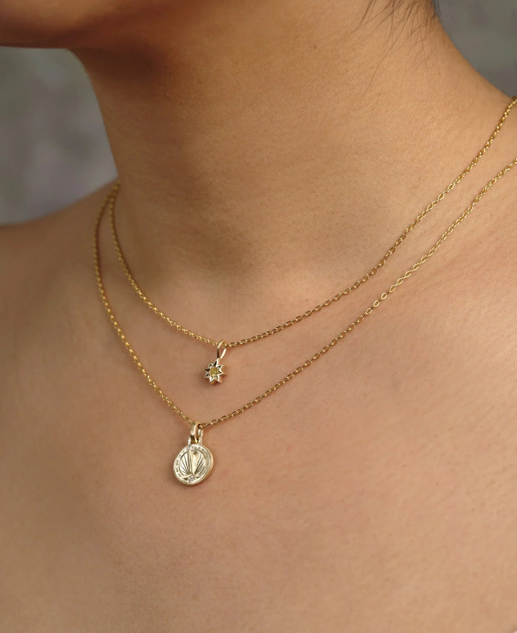 Close-up of layered delicate gold necklaces with sunburst and coin pendants on natural skin