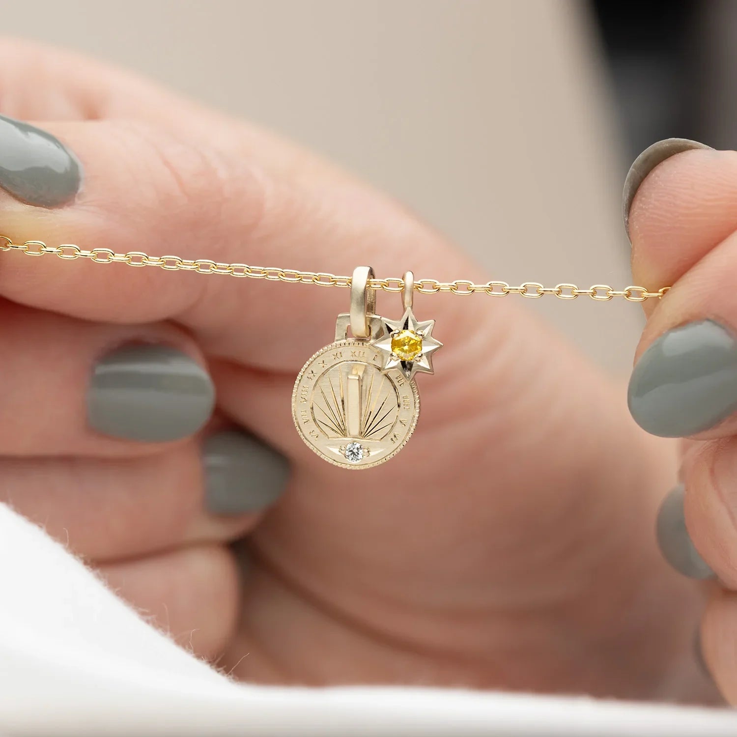 Hand holding gold sundial pendant and star charm with gemstone on delicate chain, soft natural light