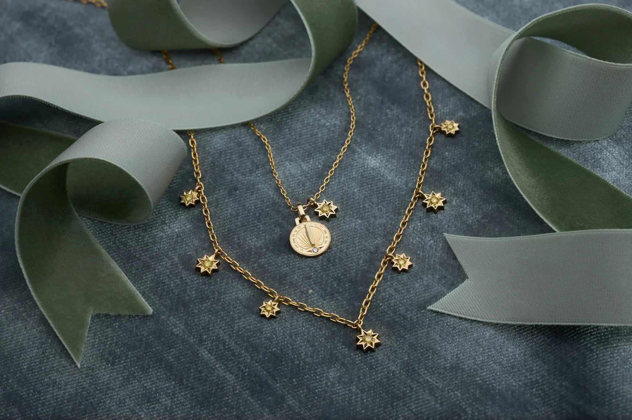 Hand-fabricated Fairmined gold sundial pendant and star charm necklace on soft grey velvet with sage green ribbon