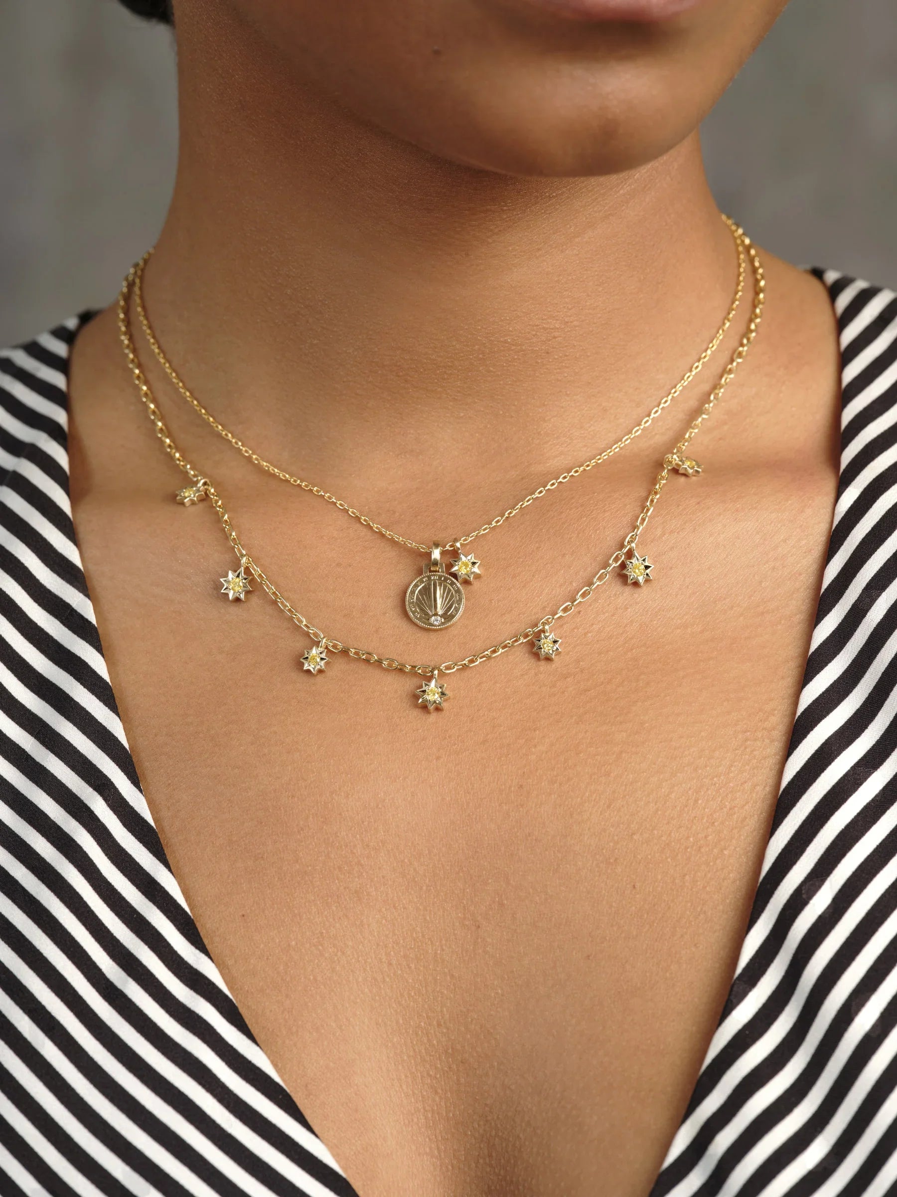 Close-up of two layered Fairmined gold necklaces on neck with delicate star charms and sundial pendant, soft natural light