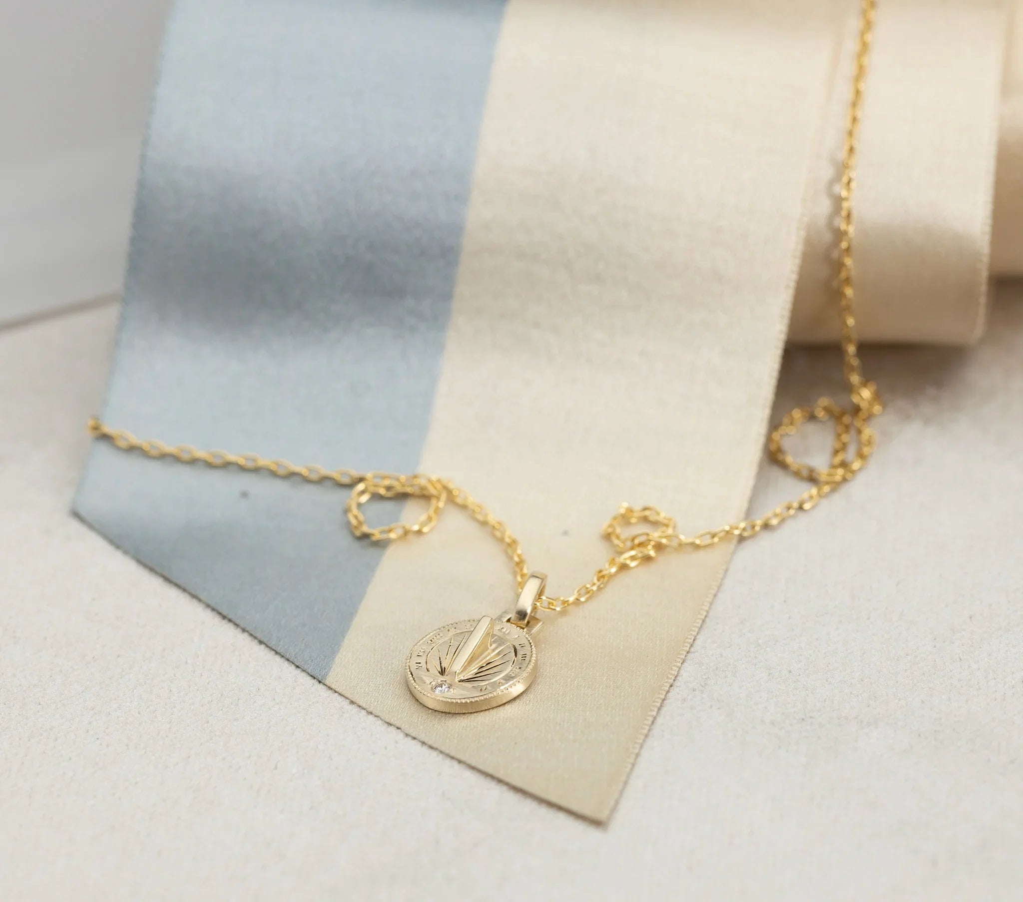 Close-up of handcrafted gold sundial necklace with diamond detail on soft beige and blue linen background