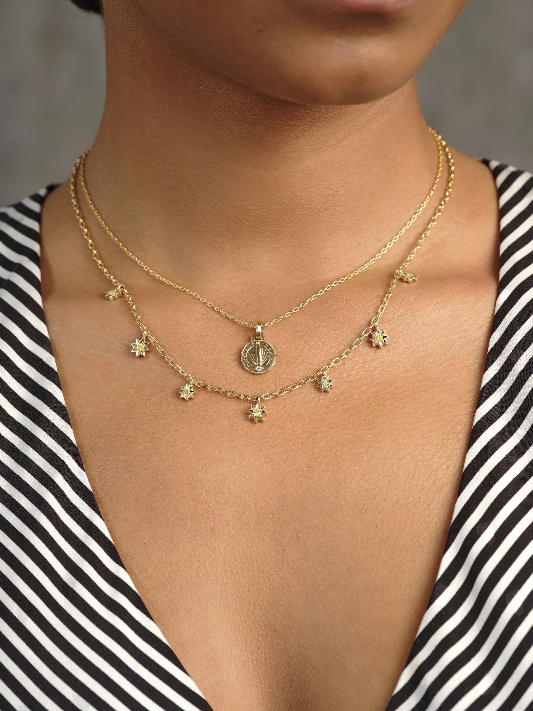 Close-up of layered Fairmined gold sundial pendant and star charm necklace on natural skin with warm lighting