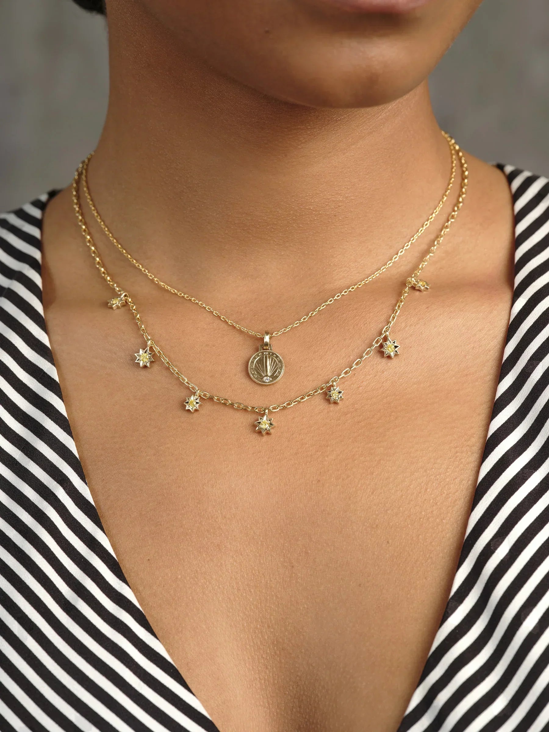 Close-up of layered Fairmined gold necklaces featuring a sundial pendant and star charms on warm skin