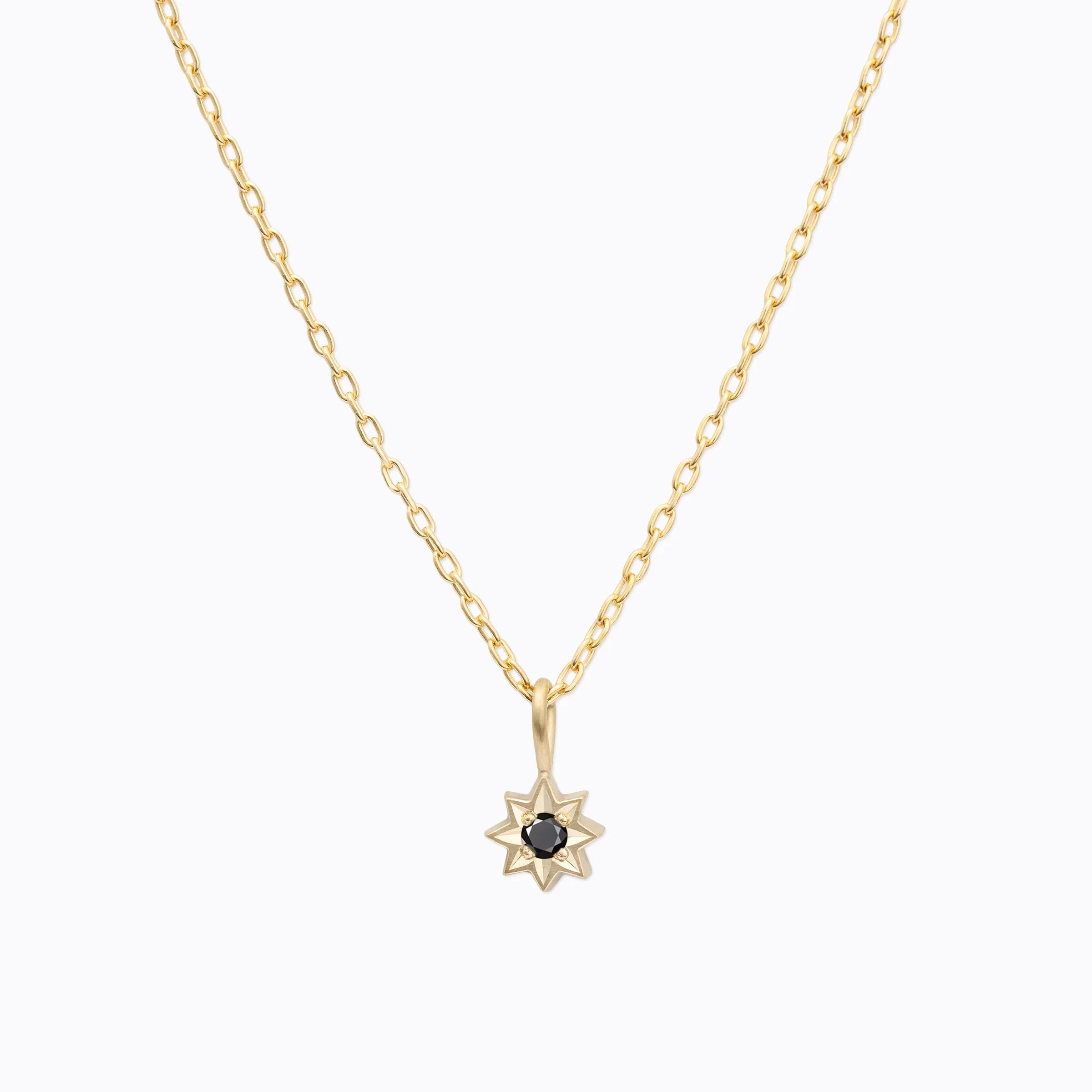 Delicate hand-fabricated Fairmined gold star pendant necklace with central black gemstone on soft white background