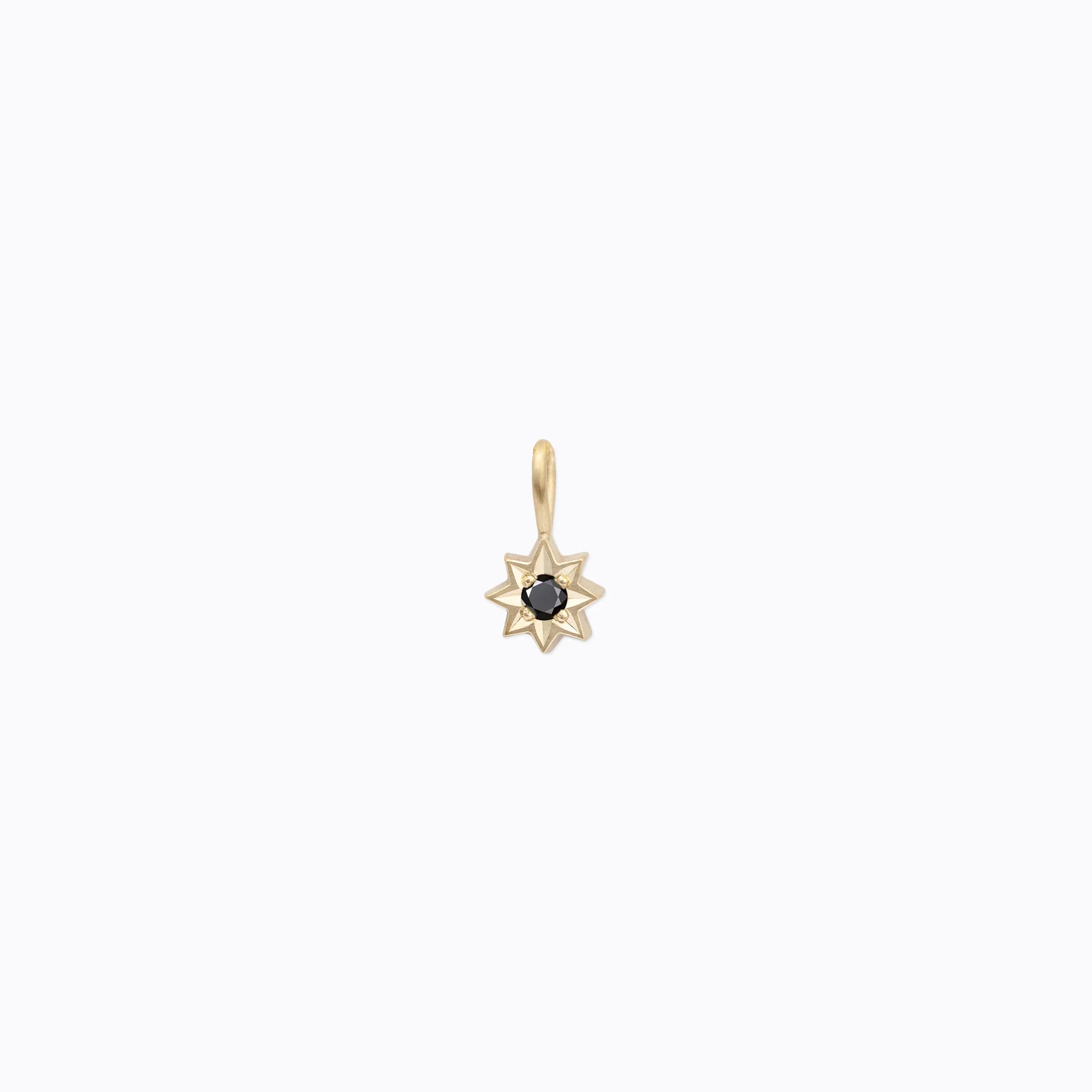 Handcrafted gold star pendant with black gemstone center on soft white background