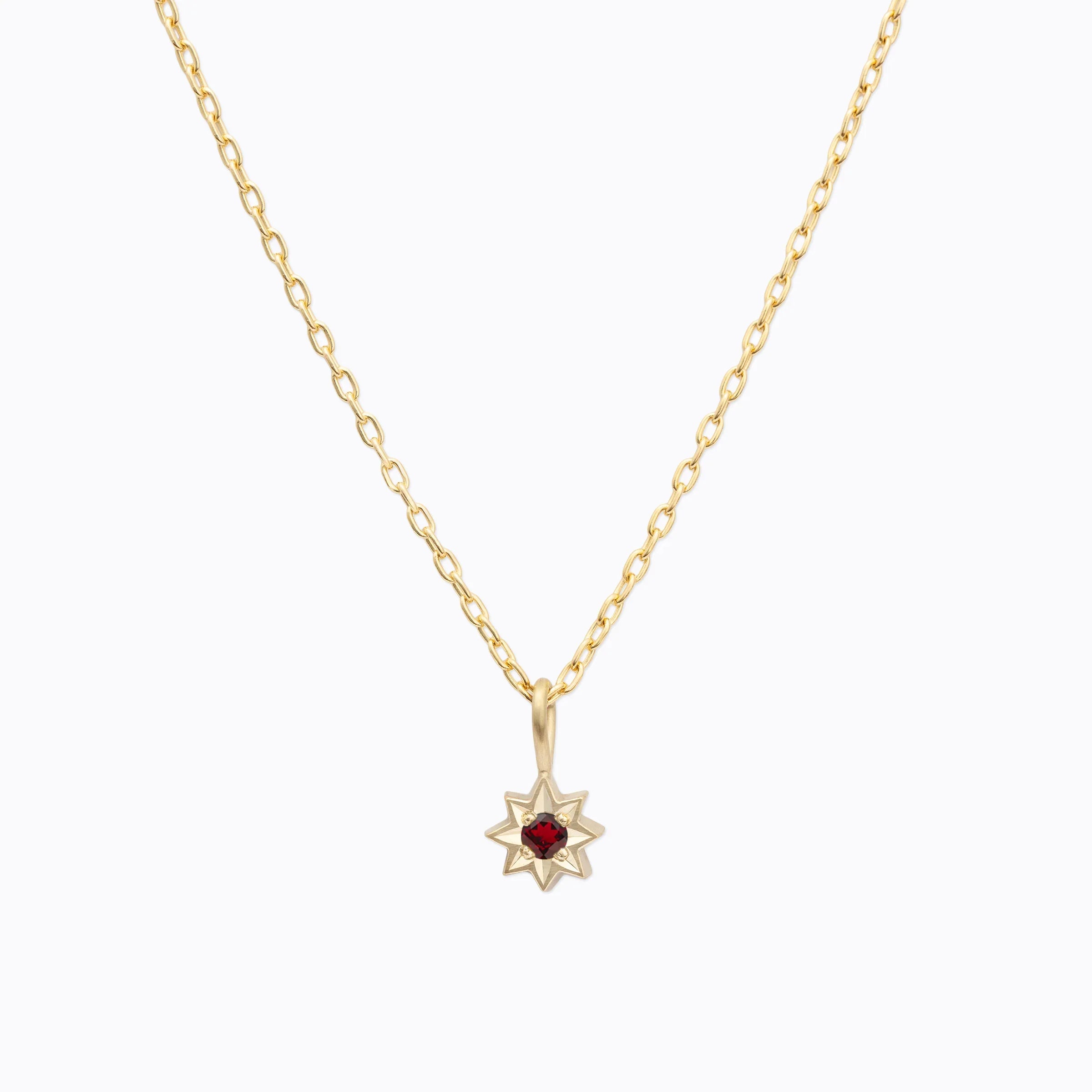 Delicate Fairmined gold star pendant necklace with red gemstone center on white background