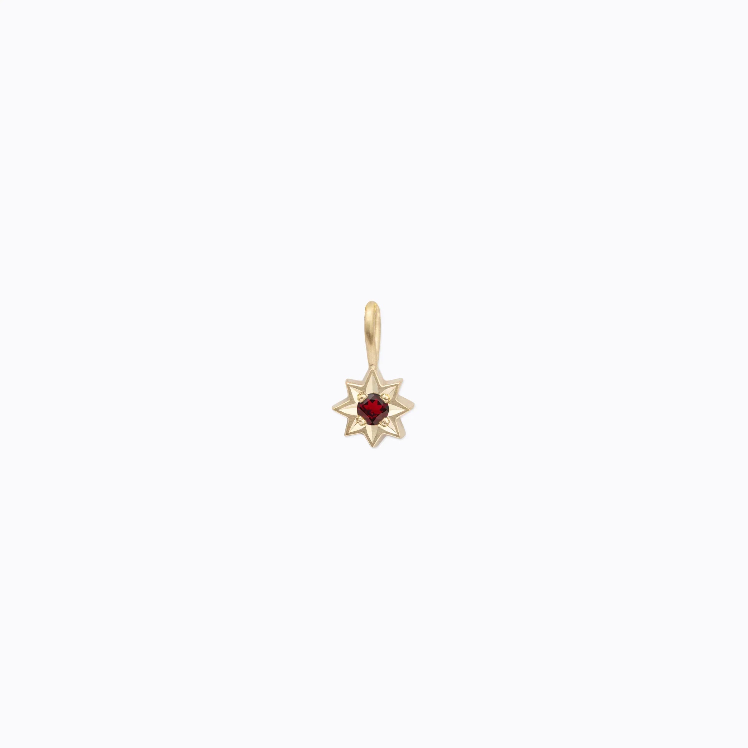 Handcrafted Fairmined gold star pendant with deep red gemstone center on soft cream background