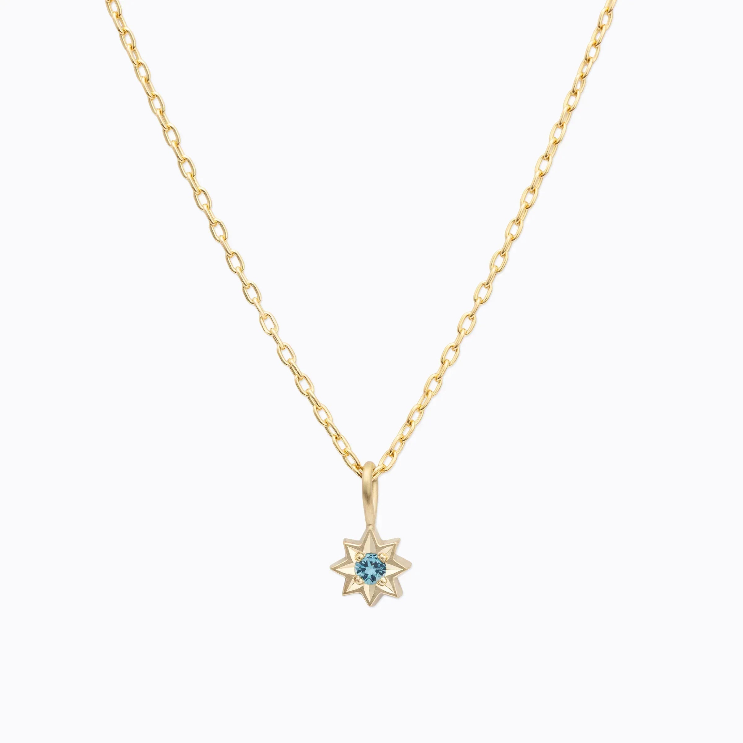 Delicate gold star pendant necklace with central blue gemstone on white background