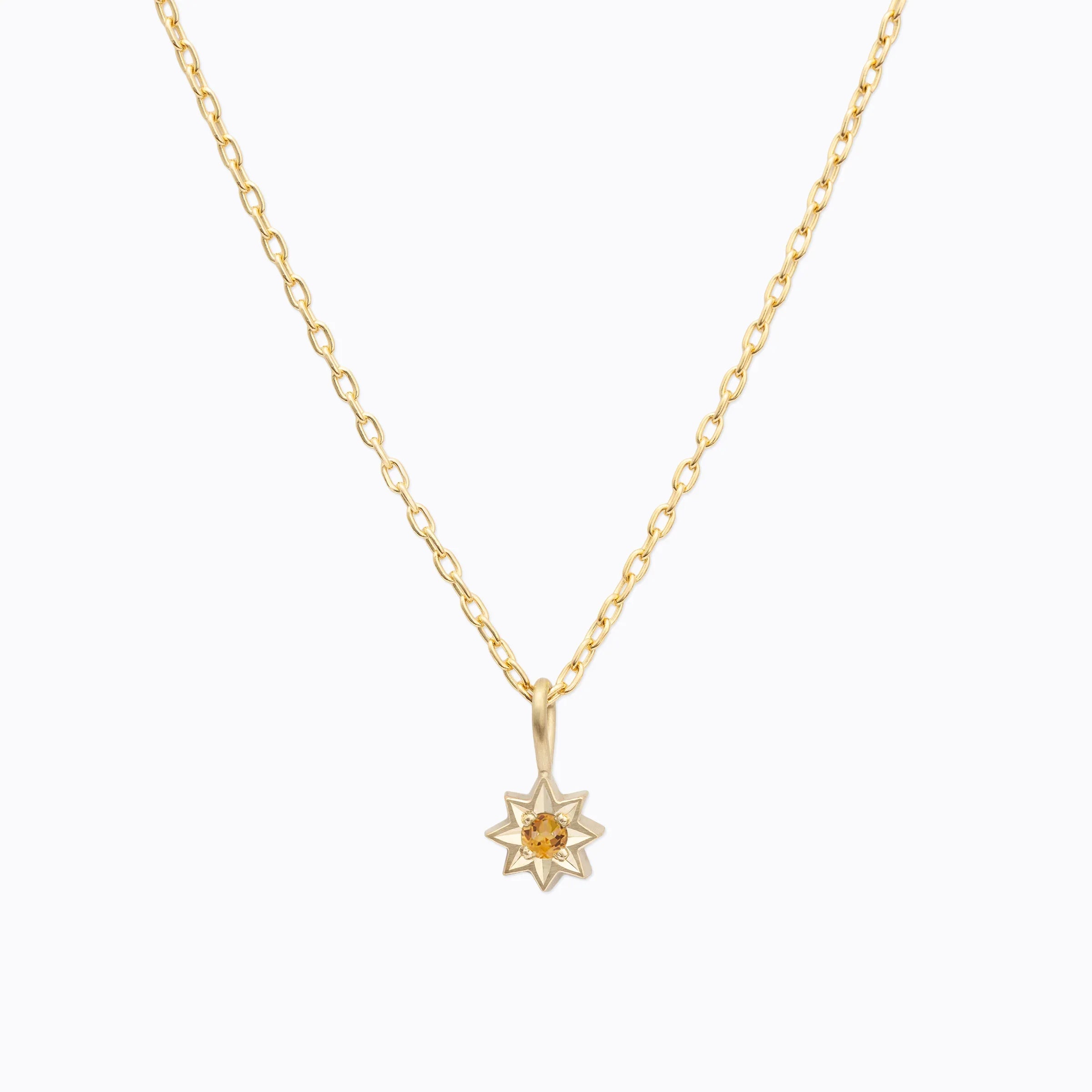 Delicate 18k gold star-shaped pendant necklace with amber gemstone on white background