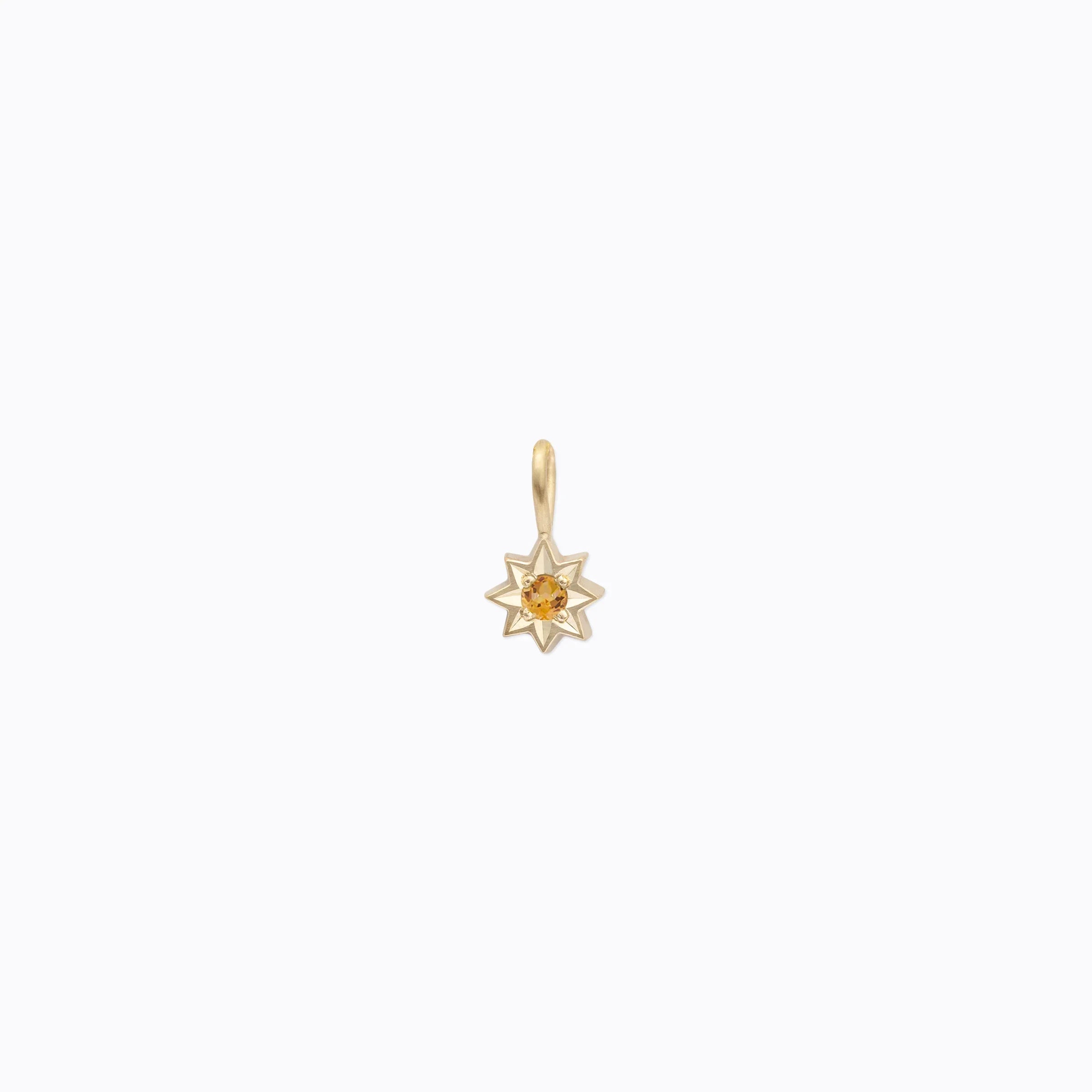 Delicate gold star pendant with orange gemstone center on soft white background
