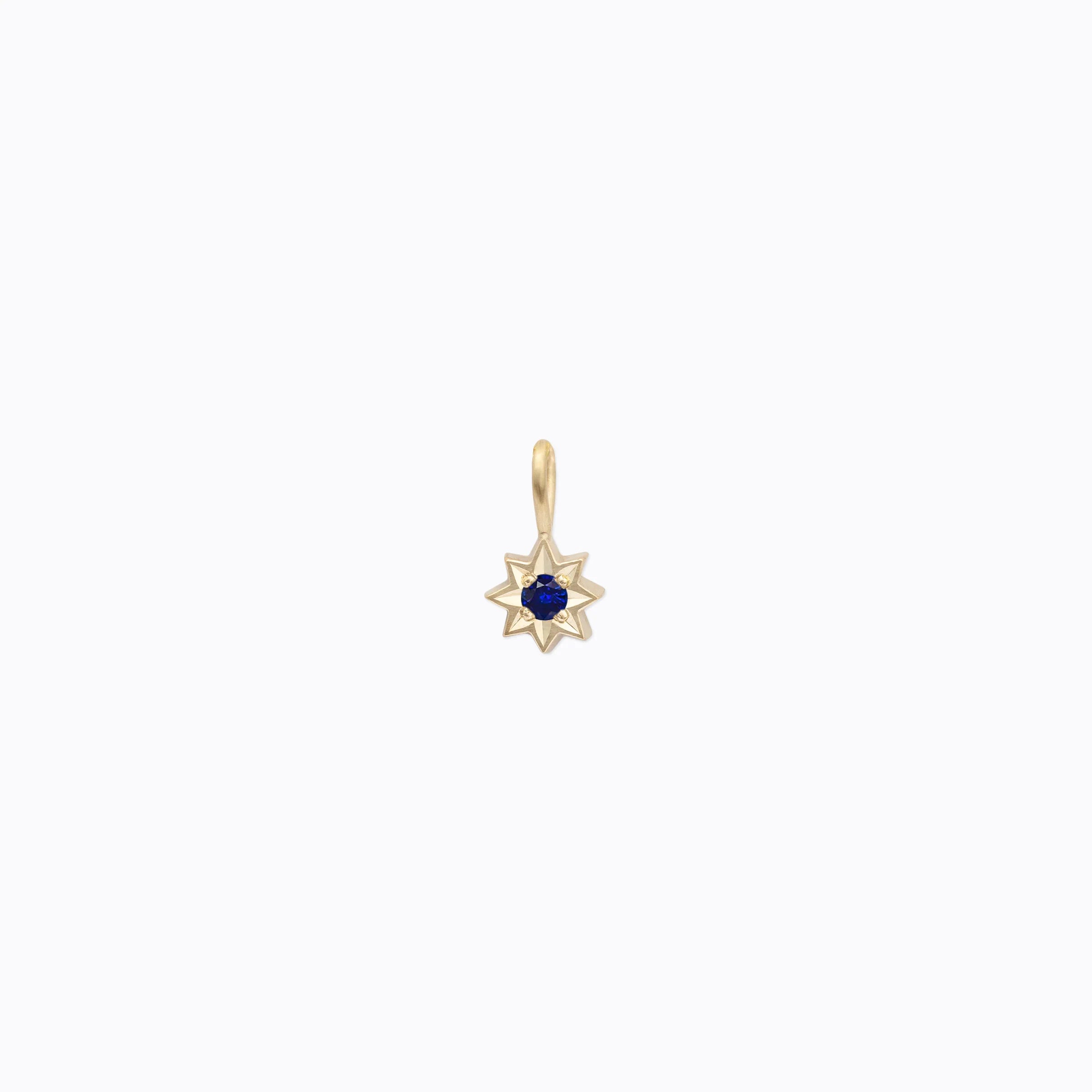 Small gold star-shaped pendant with deep blue gemstone in center on clean white background