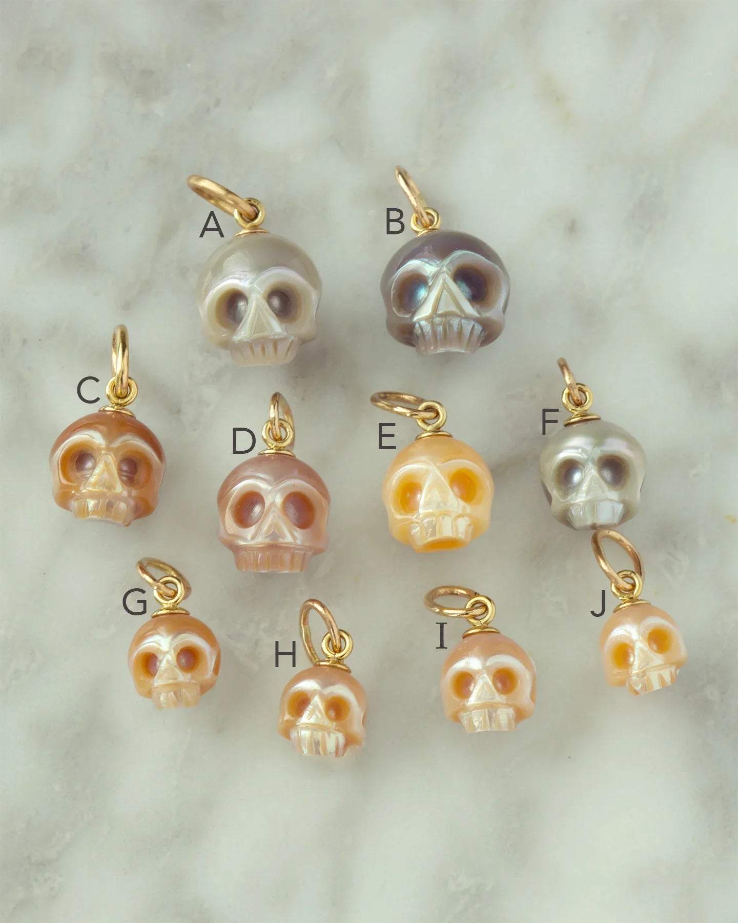 Group of ten small pearl skull charms with gold loops on soft marble surface, warm natural light
