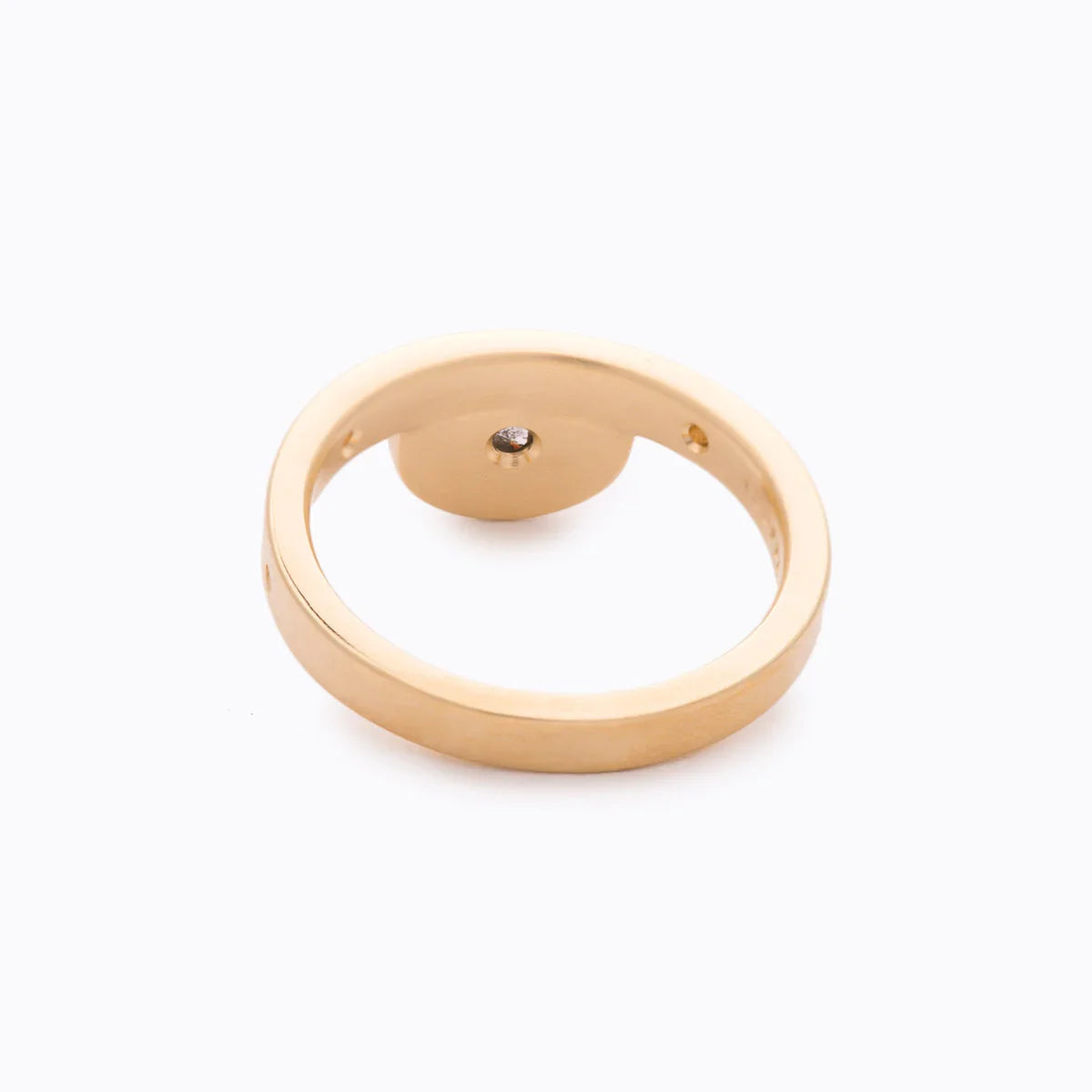 Minimalist gold ring with raised circular centerpiece and diamond detail on white background