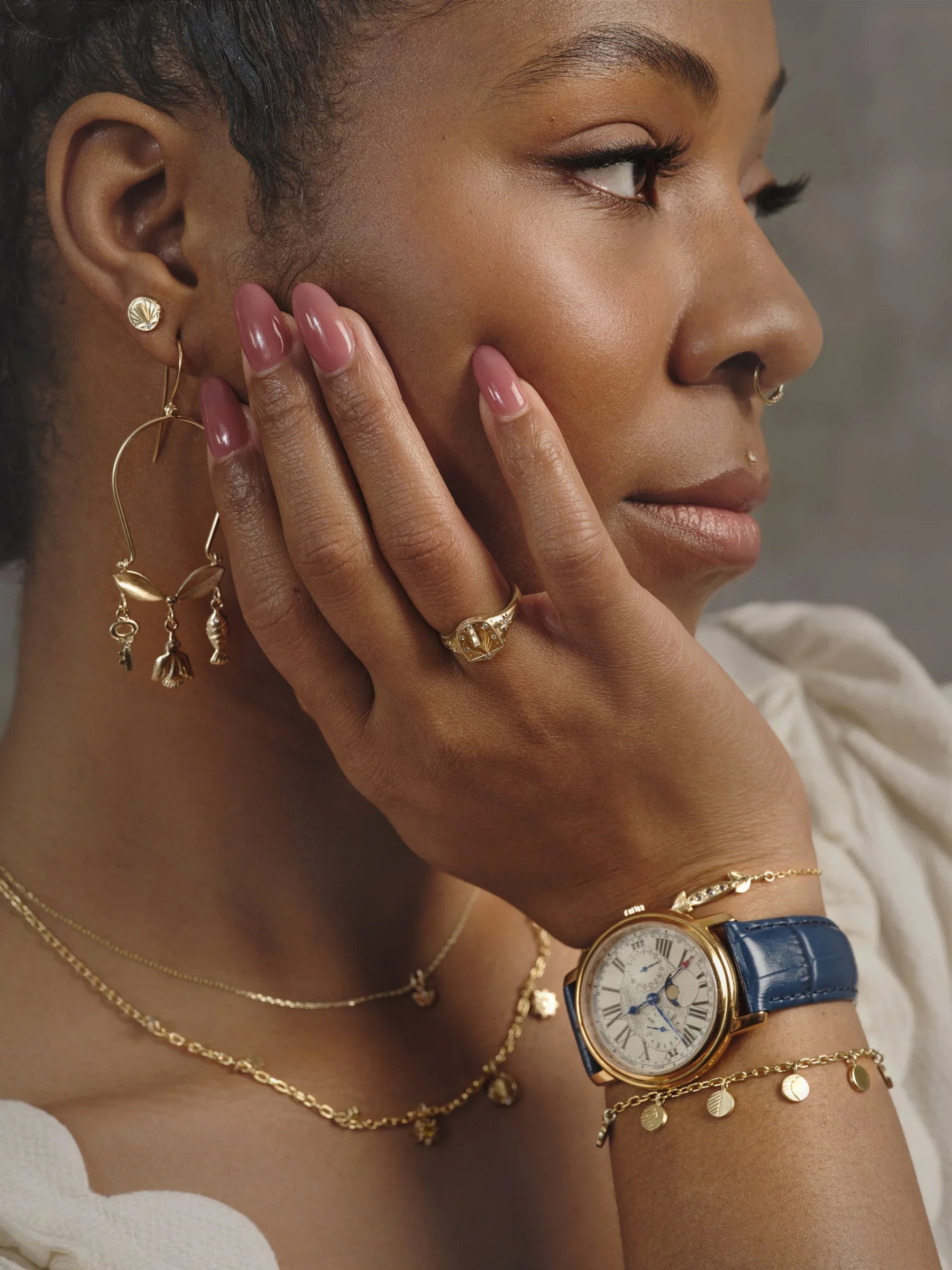 Woman wearing elegant gold handcrafted jewelry including moon phase watch with blue strap, rings, earrings, and layered necklaces