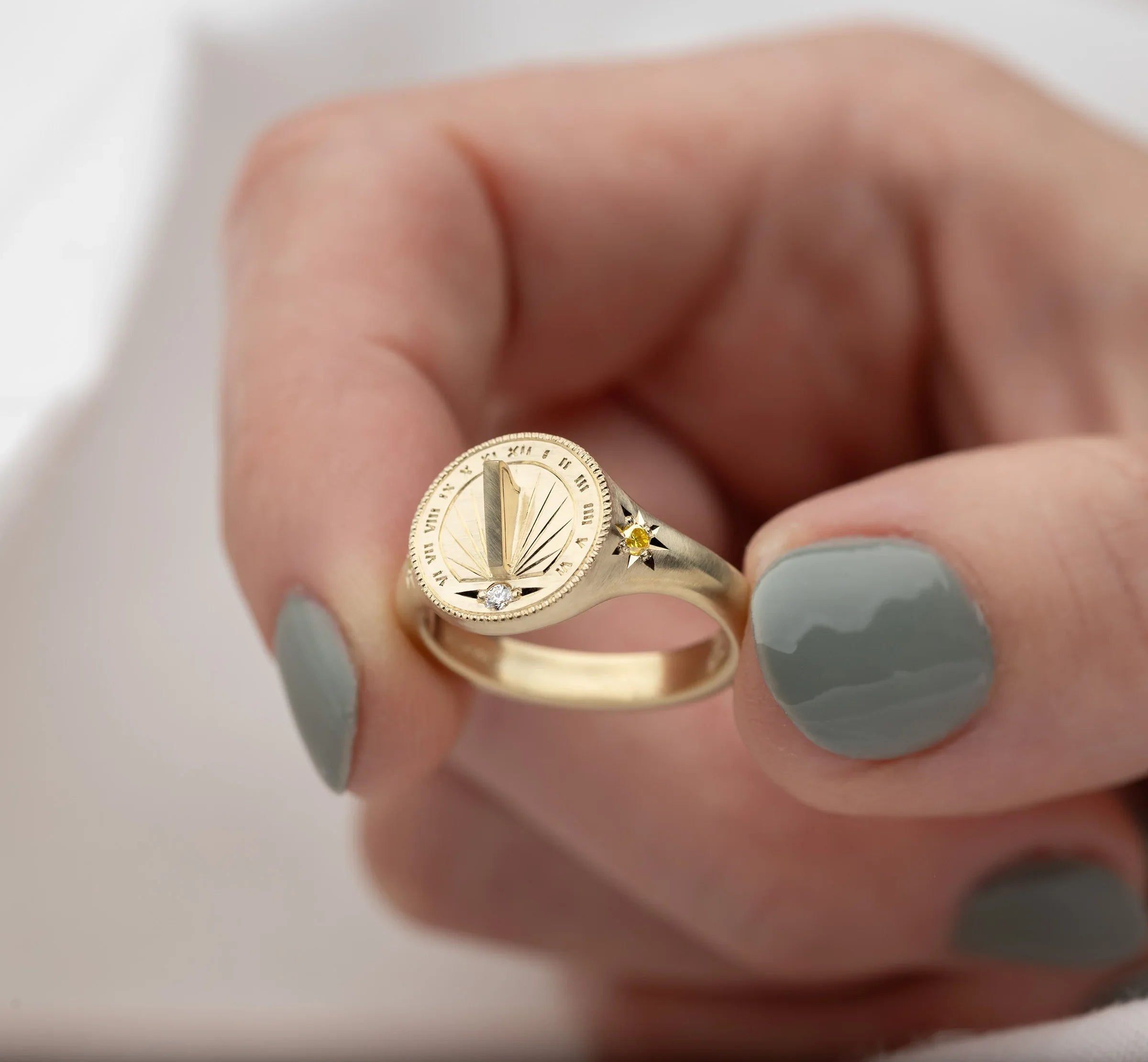 Close-up of hand holding Fairmined gold sundial ring with hand-engraved Roman numerals and small diamonds