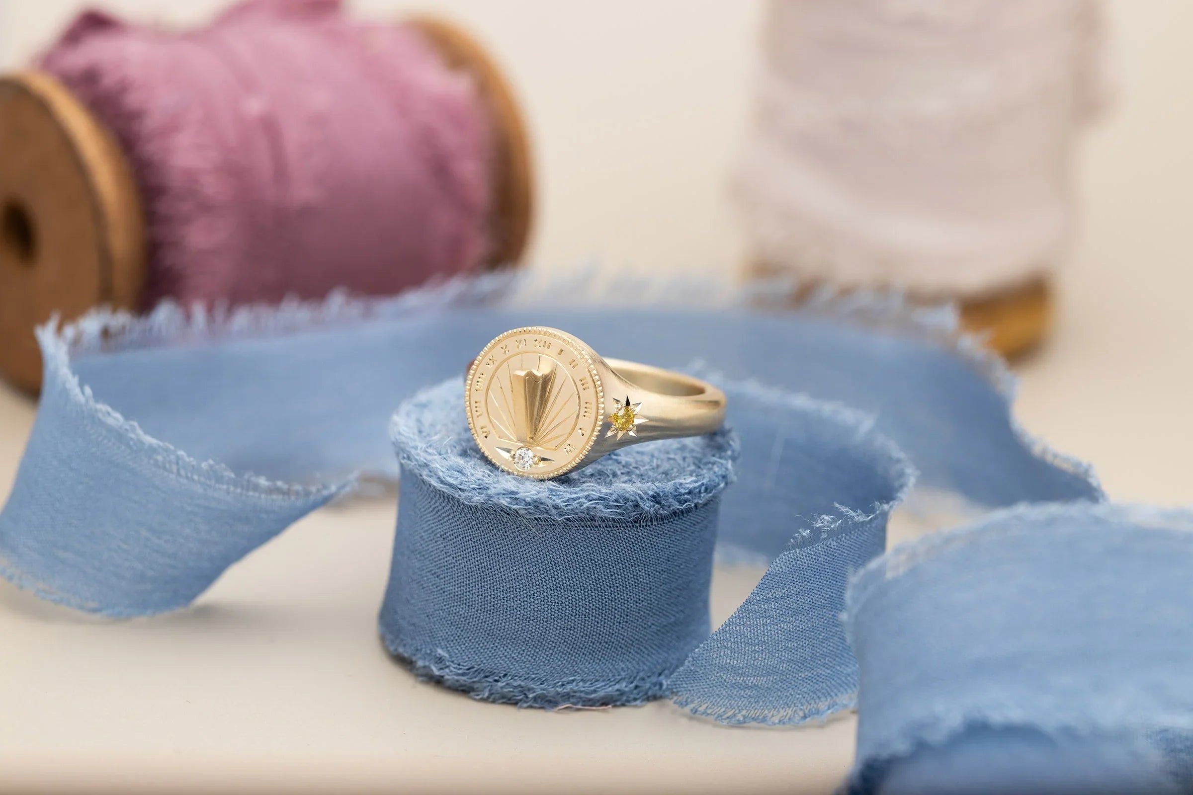 Fairmined gold sundial ring with diamond and sun motif, on natural frayed blue linen ribbon