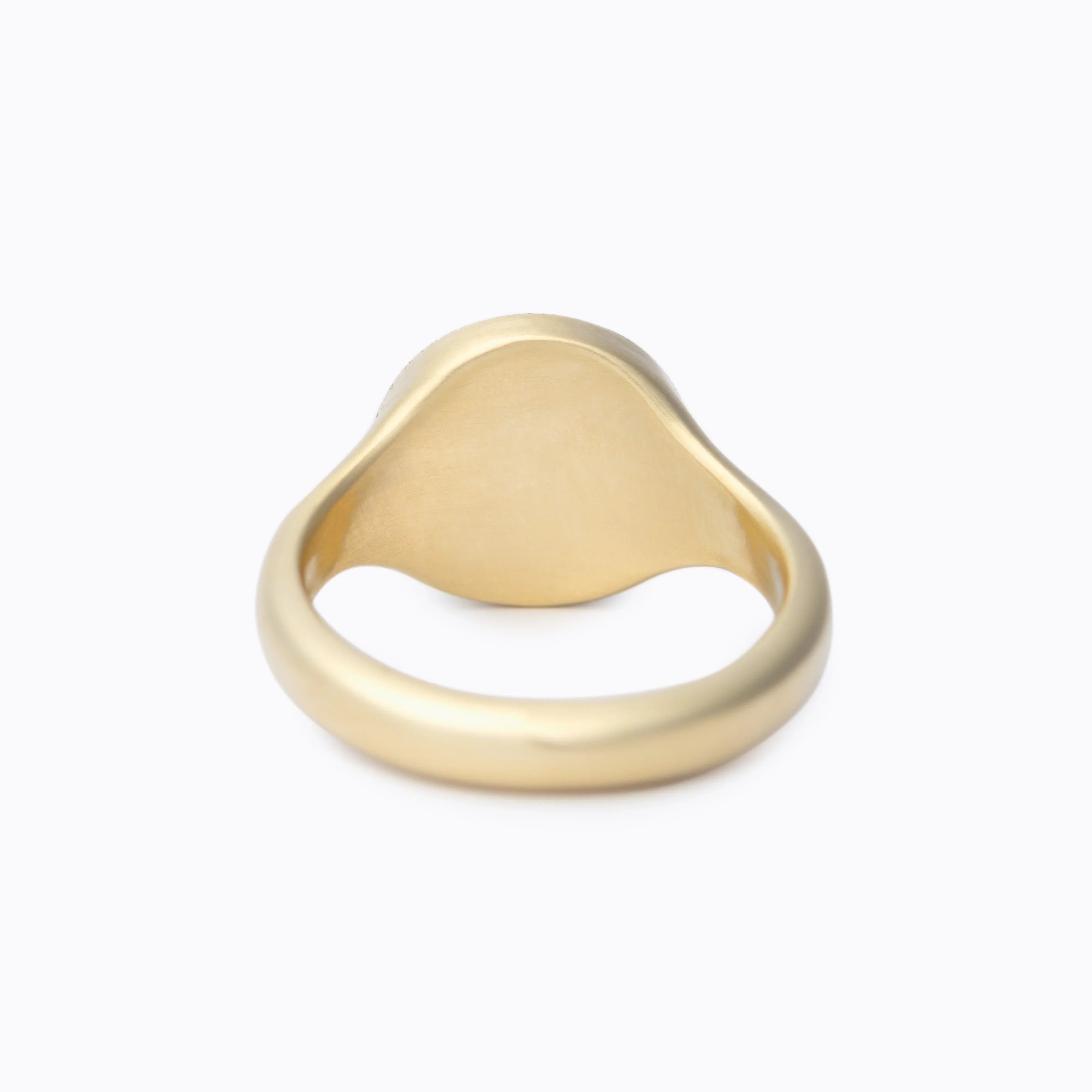 Close-up of elegant matte gold signet ring on soft white background with warm lighting