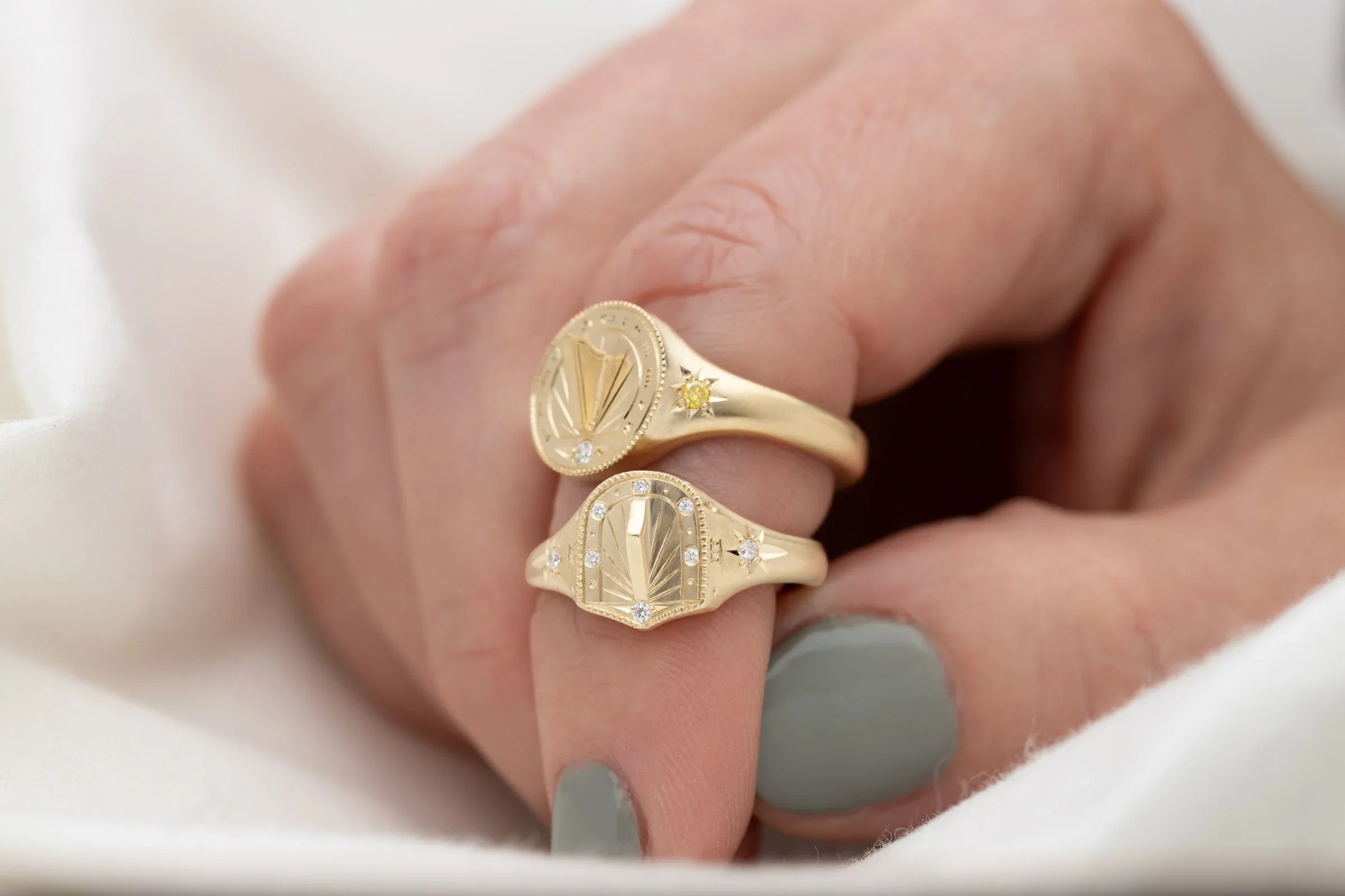 Close-up of hand-fabricated Fairmined gold sundial rings with hand-engraved details and diamonds, soft natural light