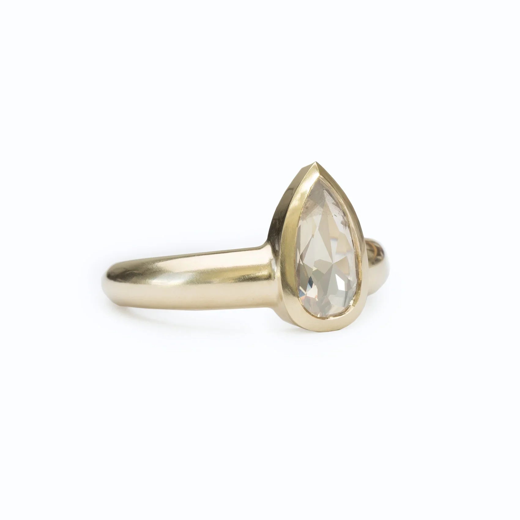 Close-up of elegant 14k yellow gold ring with pear-shaped diamond, minimalist white background
