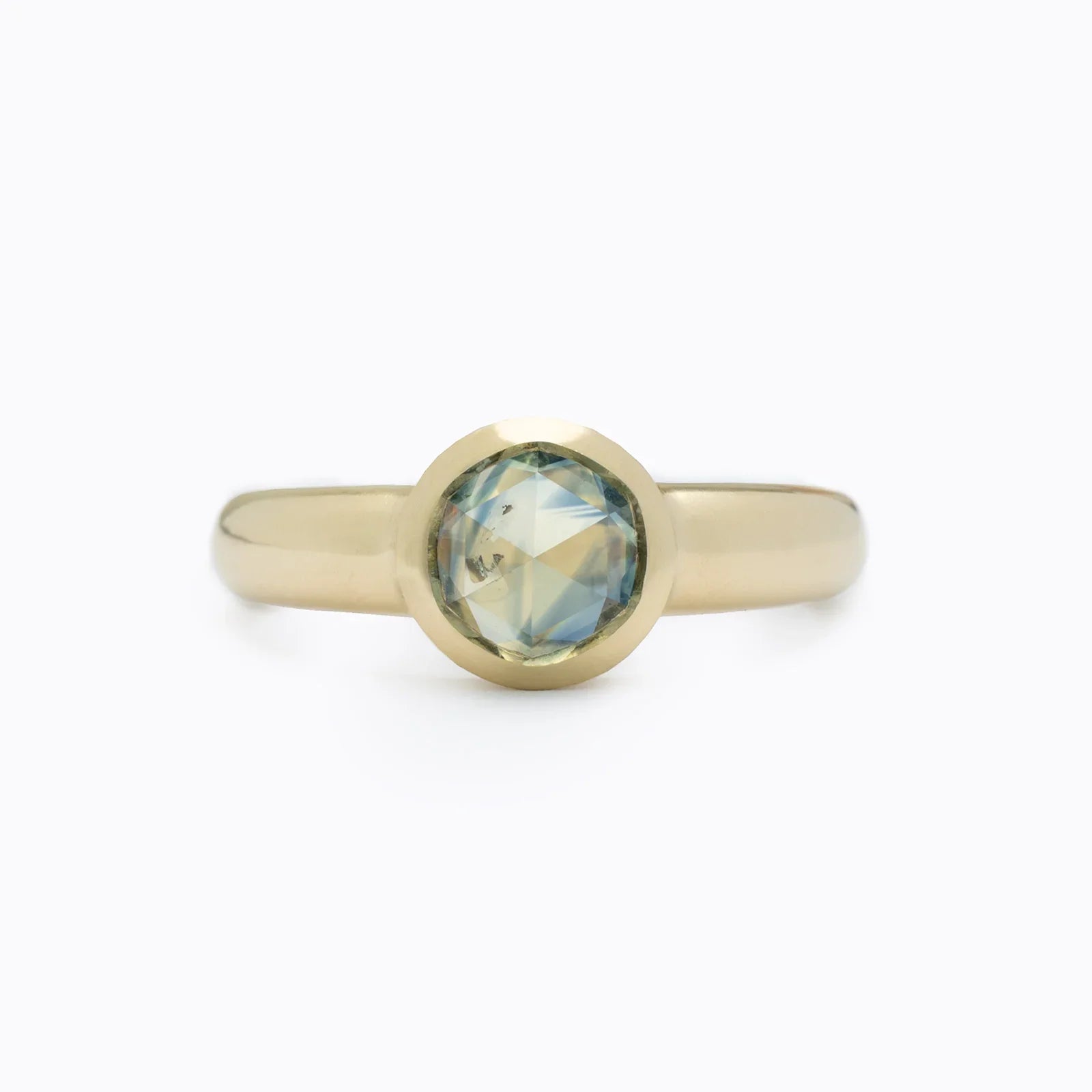 Close-up of 14k yellow gold ring with 1.25ct round sapphire, clean white background, soft natural lighting