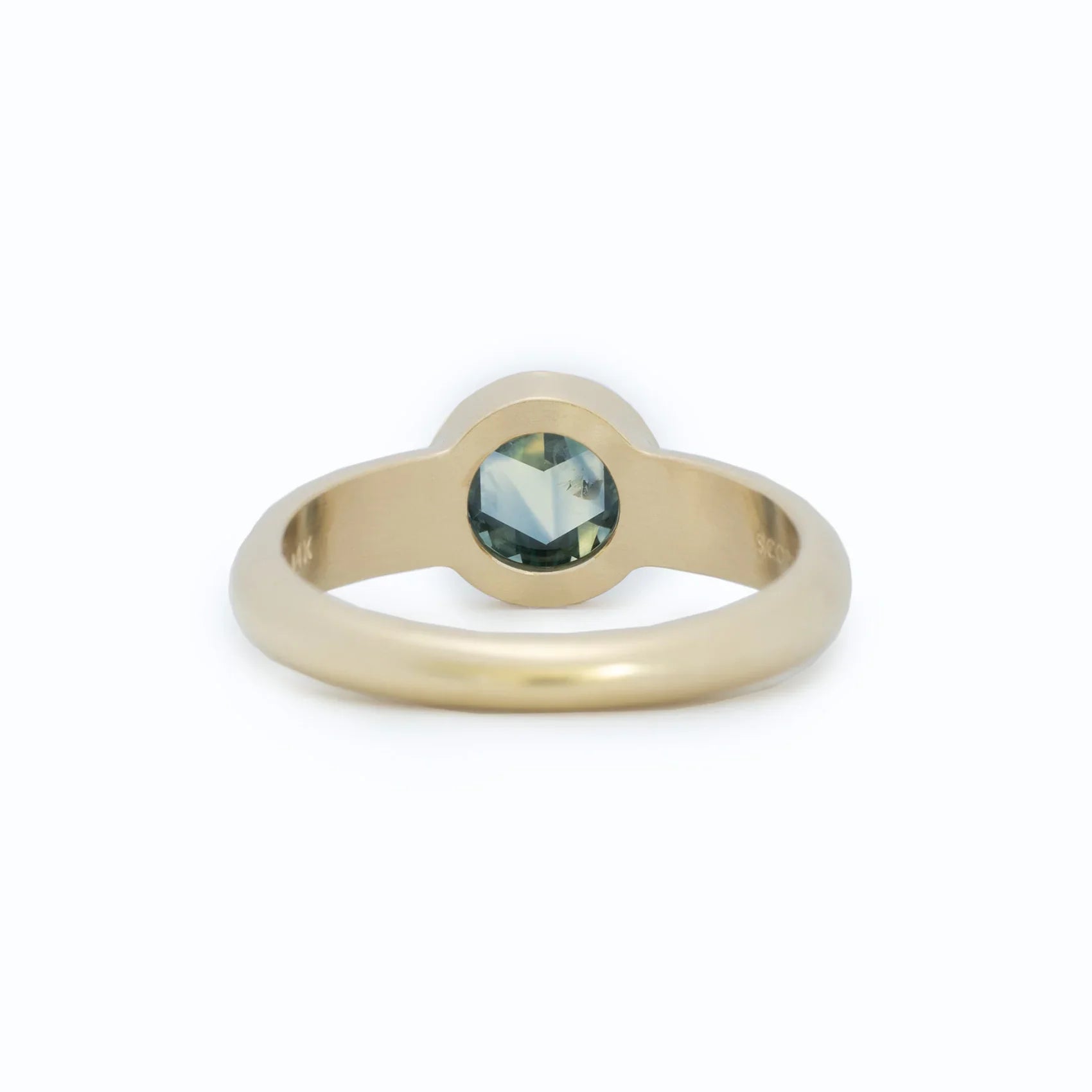 Close-up of handcrafted 14k gold ring with bezel-set green sapphire against soft white background