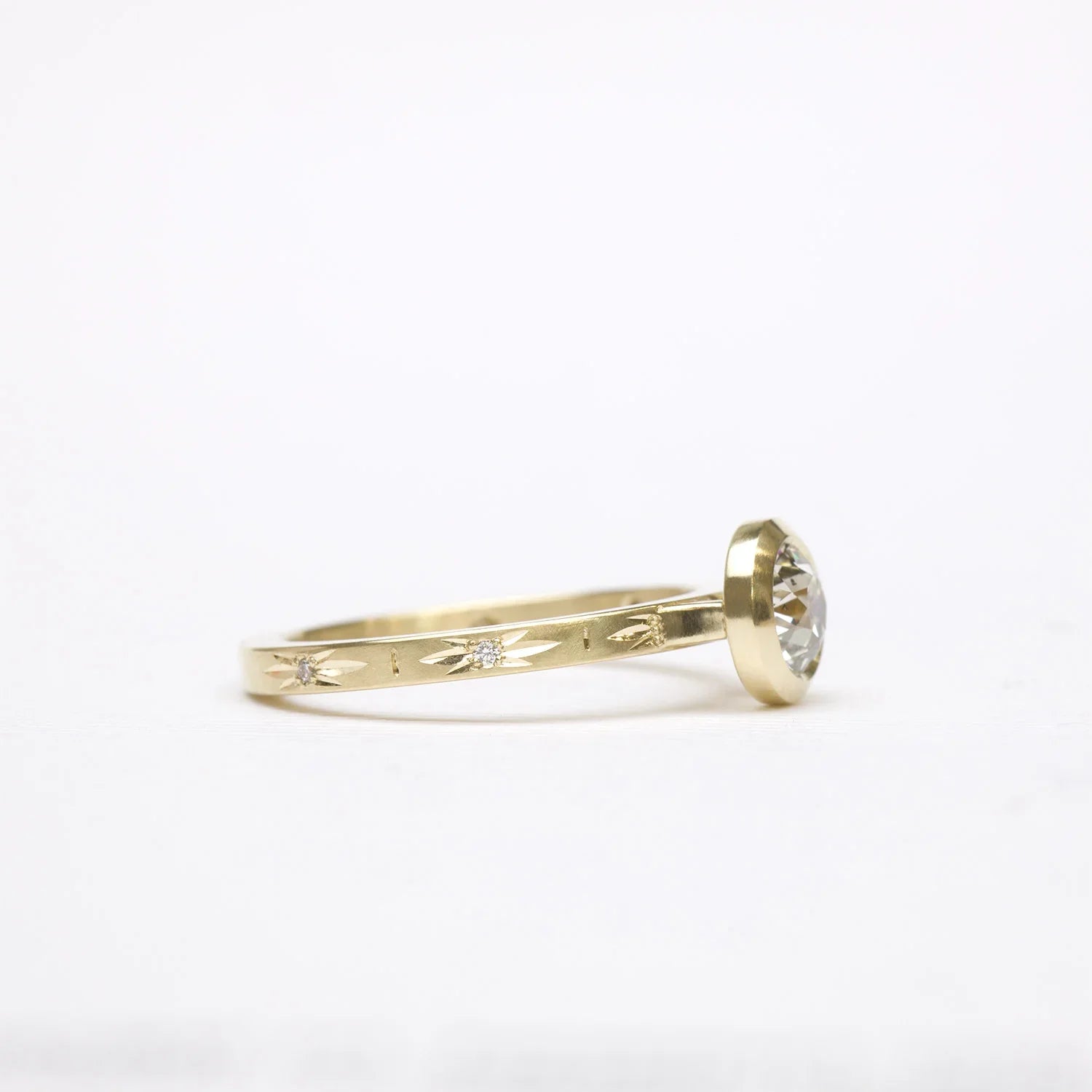 Elegant 14k gold ring with bezel-set diamond and hand-engraved starburst details on soft white background