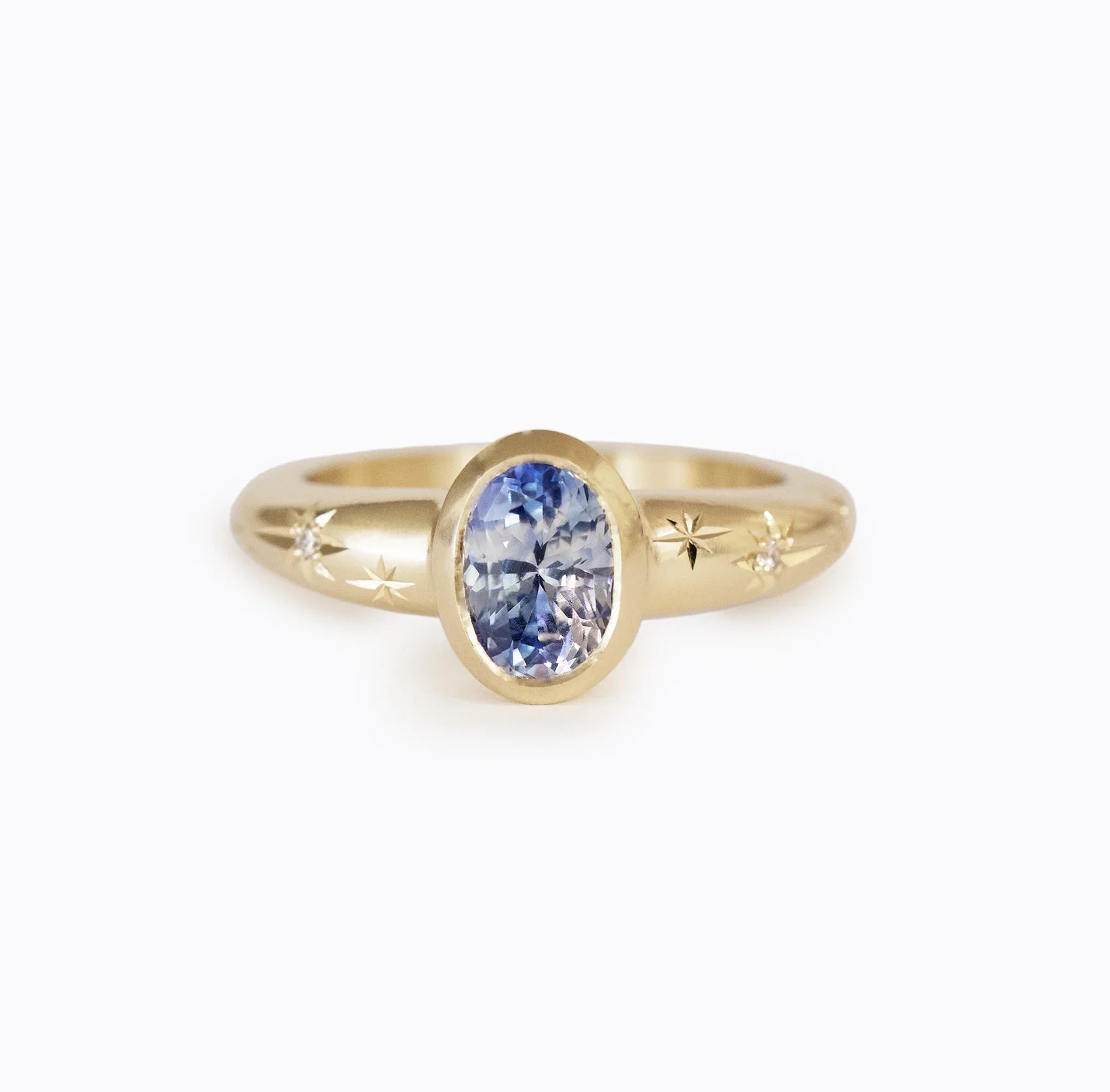 Elegant 14k gold ring with faceted oval blue sapphire and hand-engraved star details on soft white background