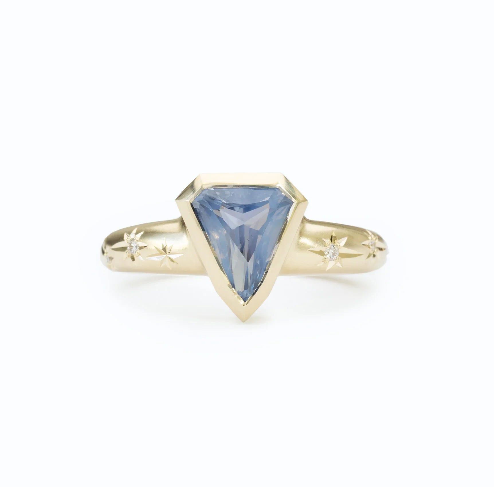 Close-up of 14k gold ring with hand-engraved star details and blue sapphire gemstone on white background