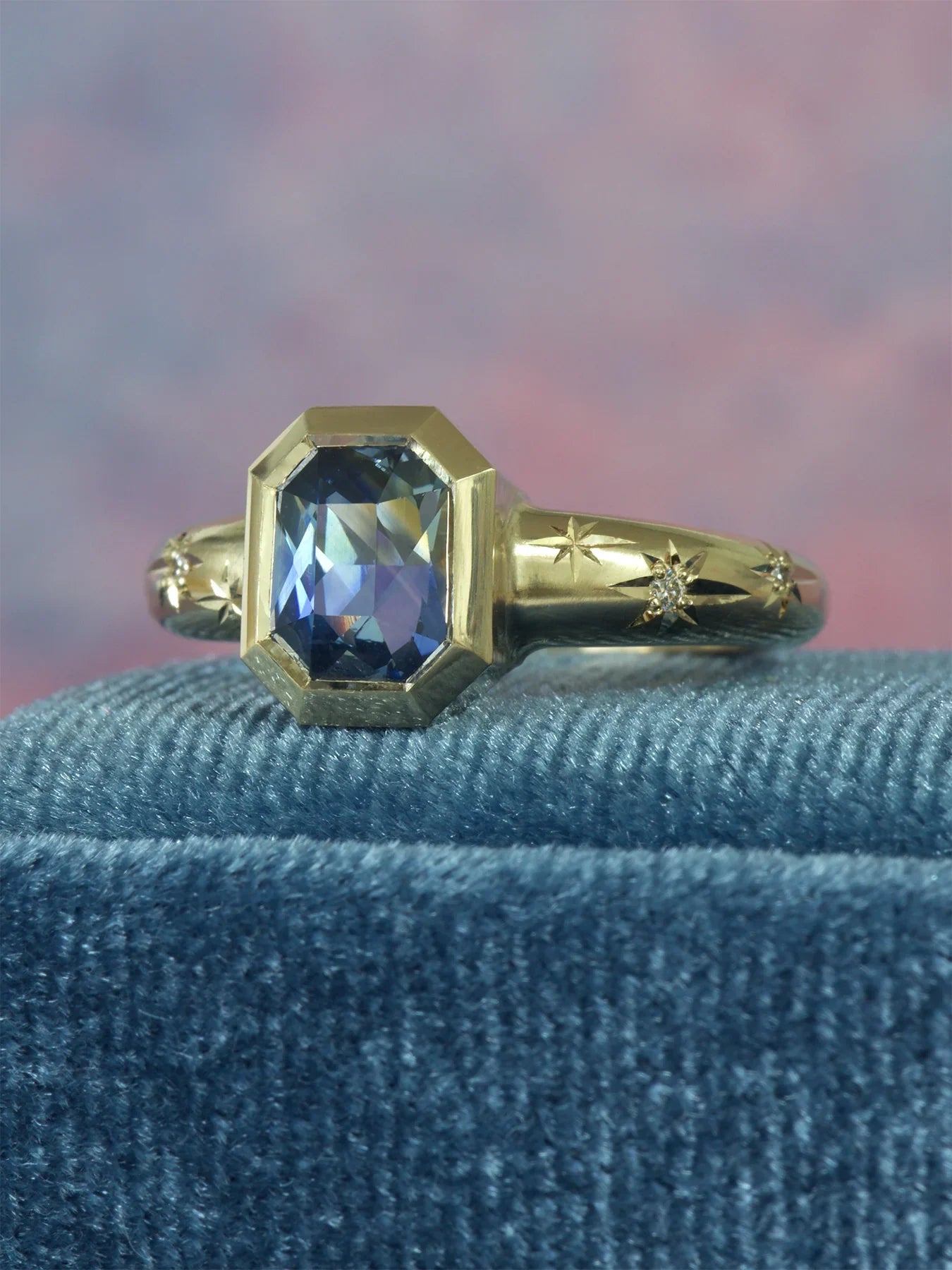 Close-up of hand-fabricated 14k gold ring with faceted sapphire and engraved star motifs on blue velvet