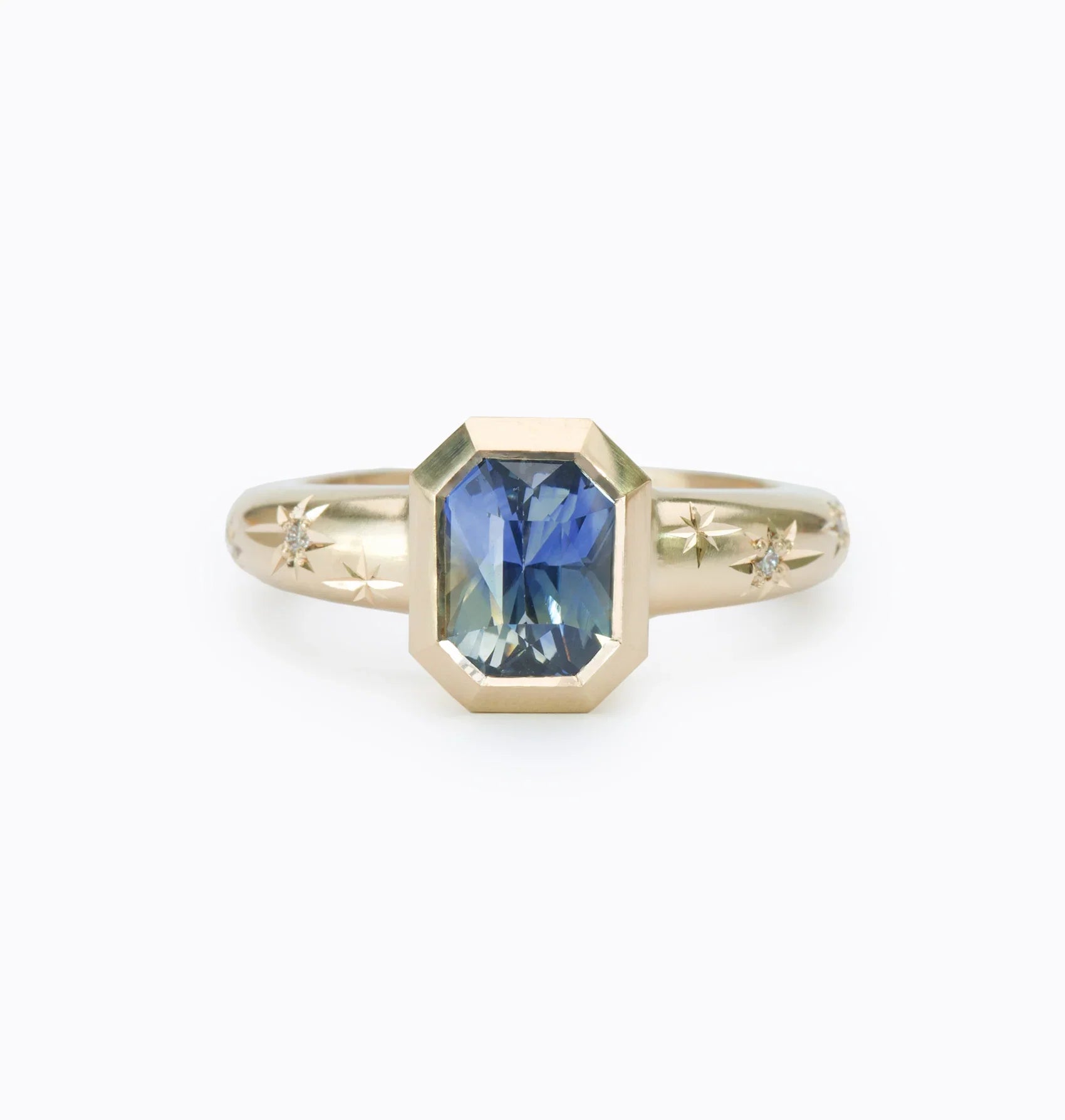 Hand-fabricated 14k gold ring with octagonal blue sapphire and hand-engraved star motifs on soft white background