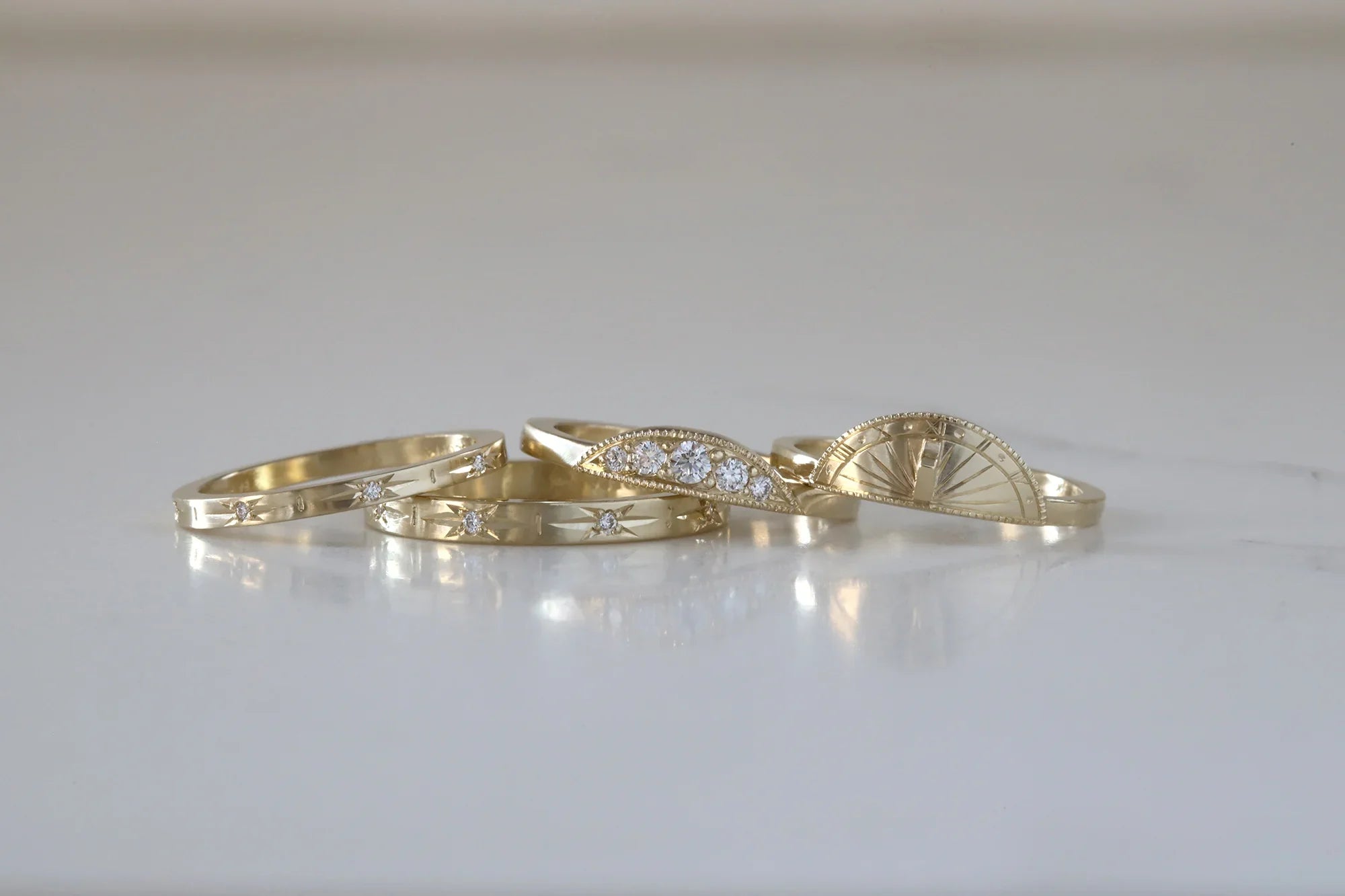 Stacked handcrafted gold rings with diamonds and sundial motif on smooth neutral surface