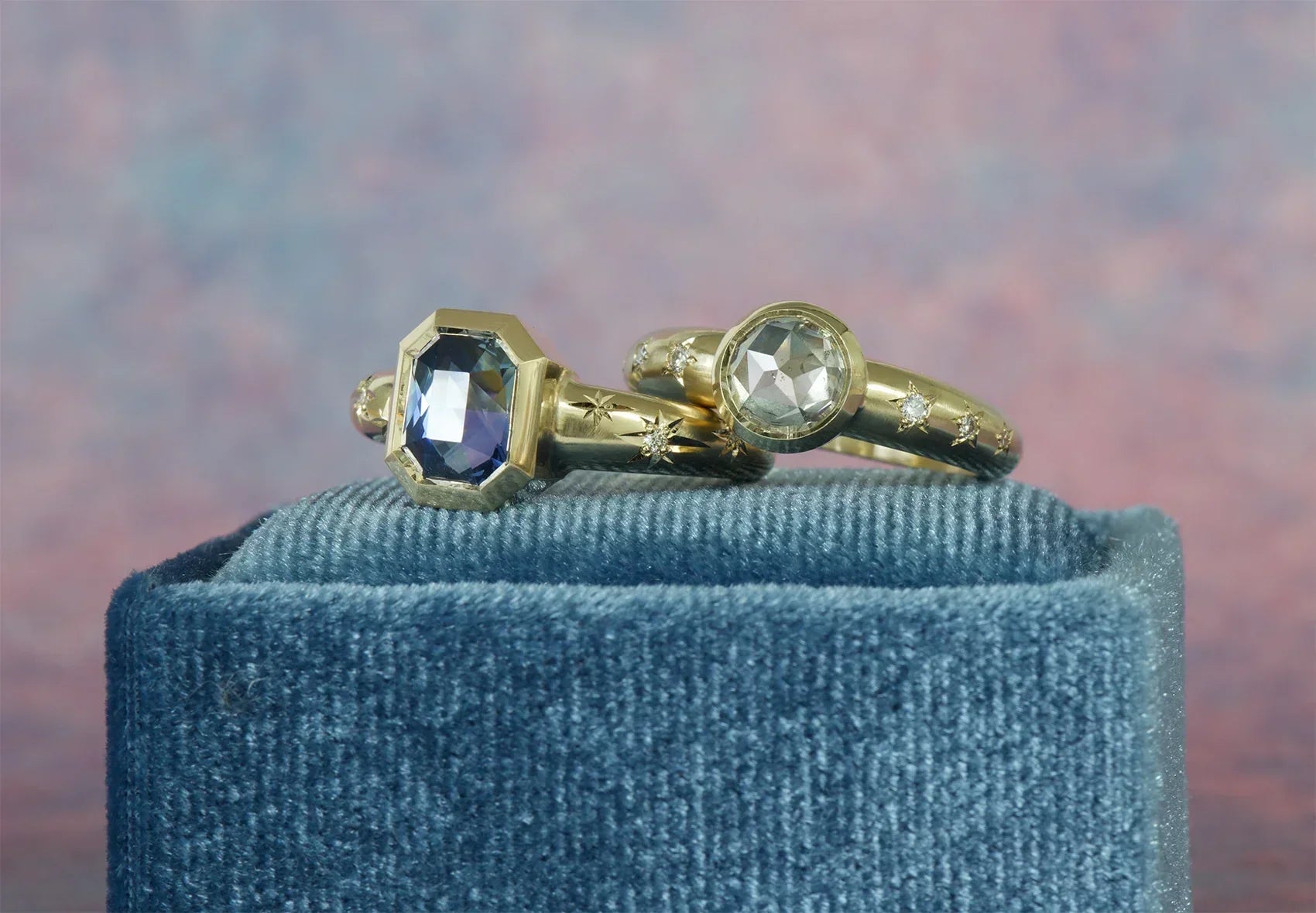 Close-up of two hand-engraved 14k gold rings with faceted gemstones and star motifs on blue velvet