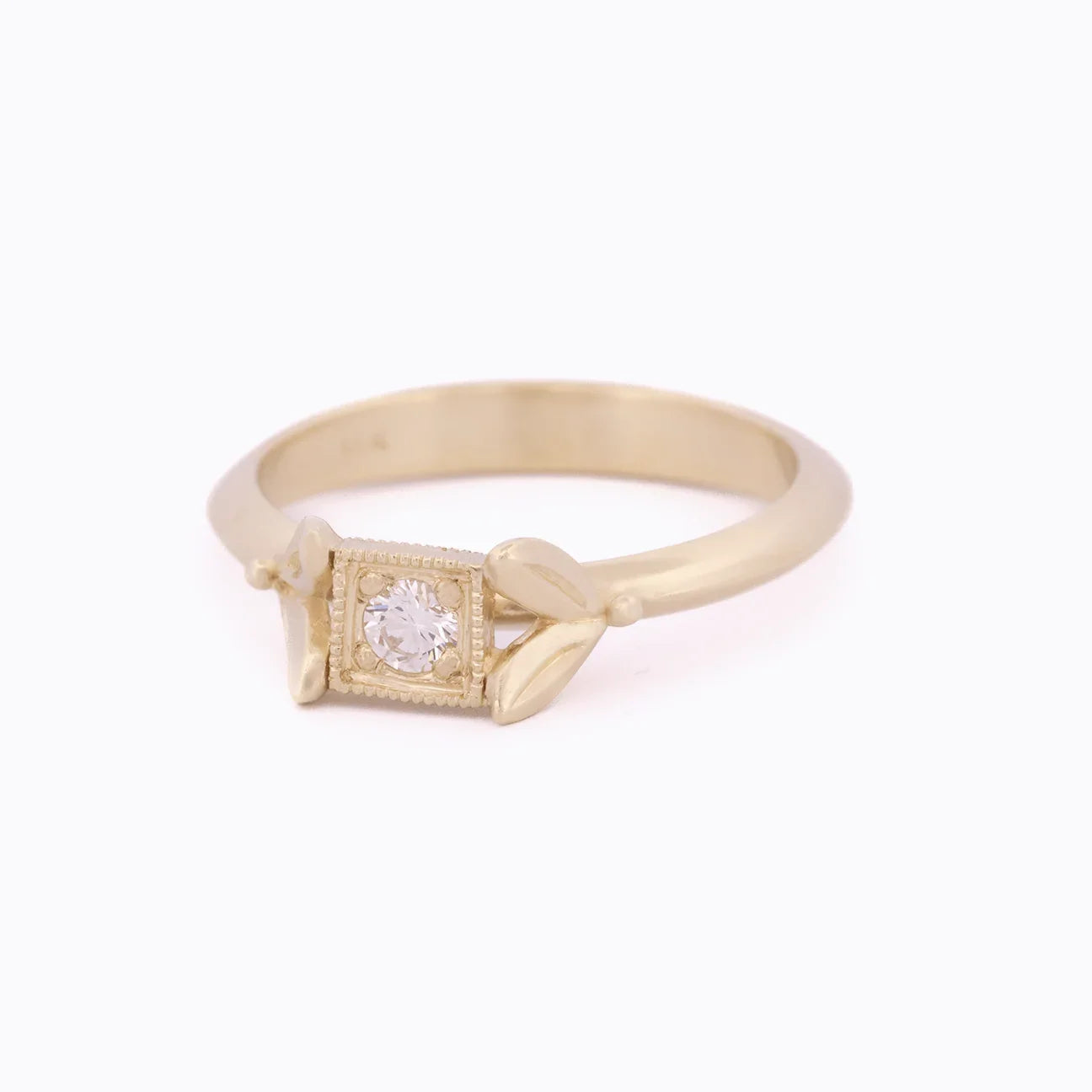 Delicate gold ring with small central diamond and leaf-inspired accents on clean white background