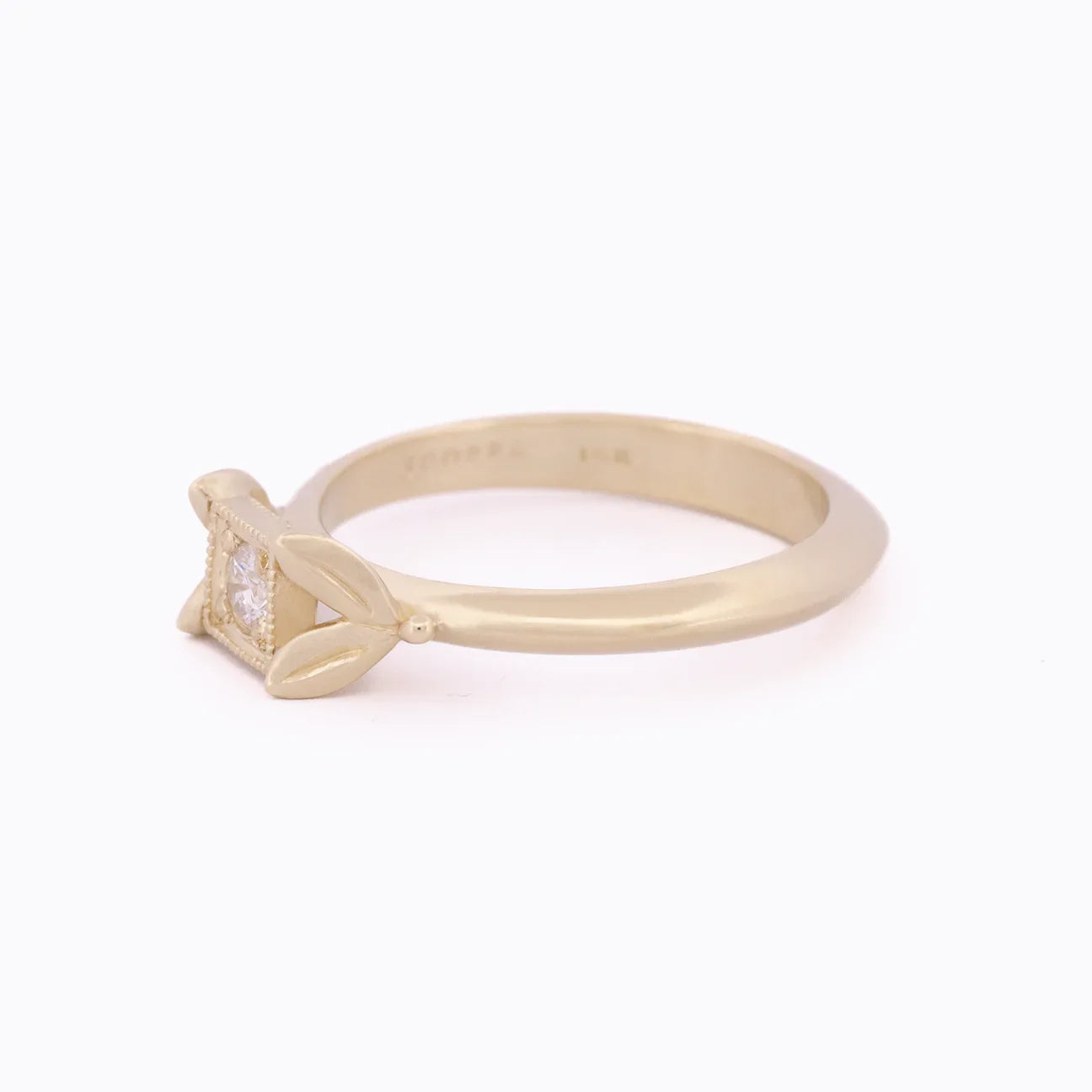 Delicate gold ring with leaf motif and square setting holding clear gemstone on white background