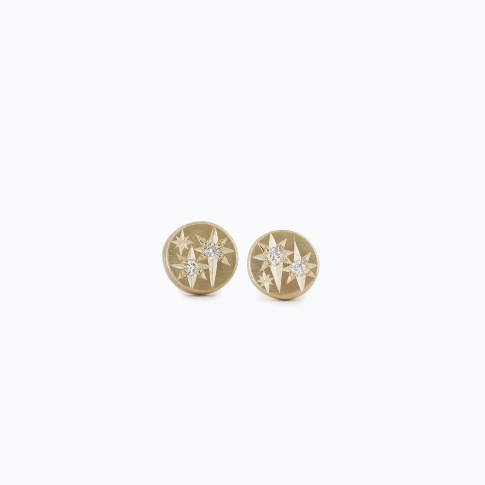 Pair of hand-engraved Fairmined gold starburst stud earrings with sparkling diamonds on white background
