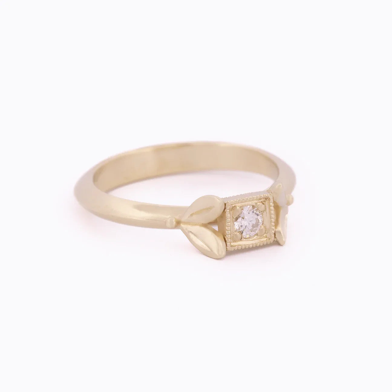 Hand-fabricated gold ring with square-cut diamond and two leaf accents on soft white background