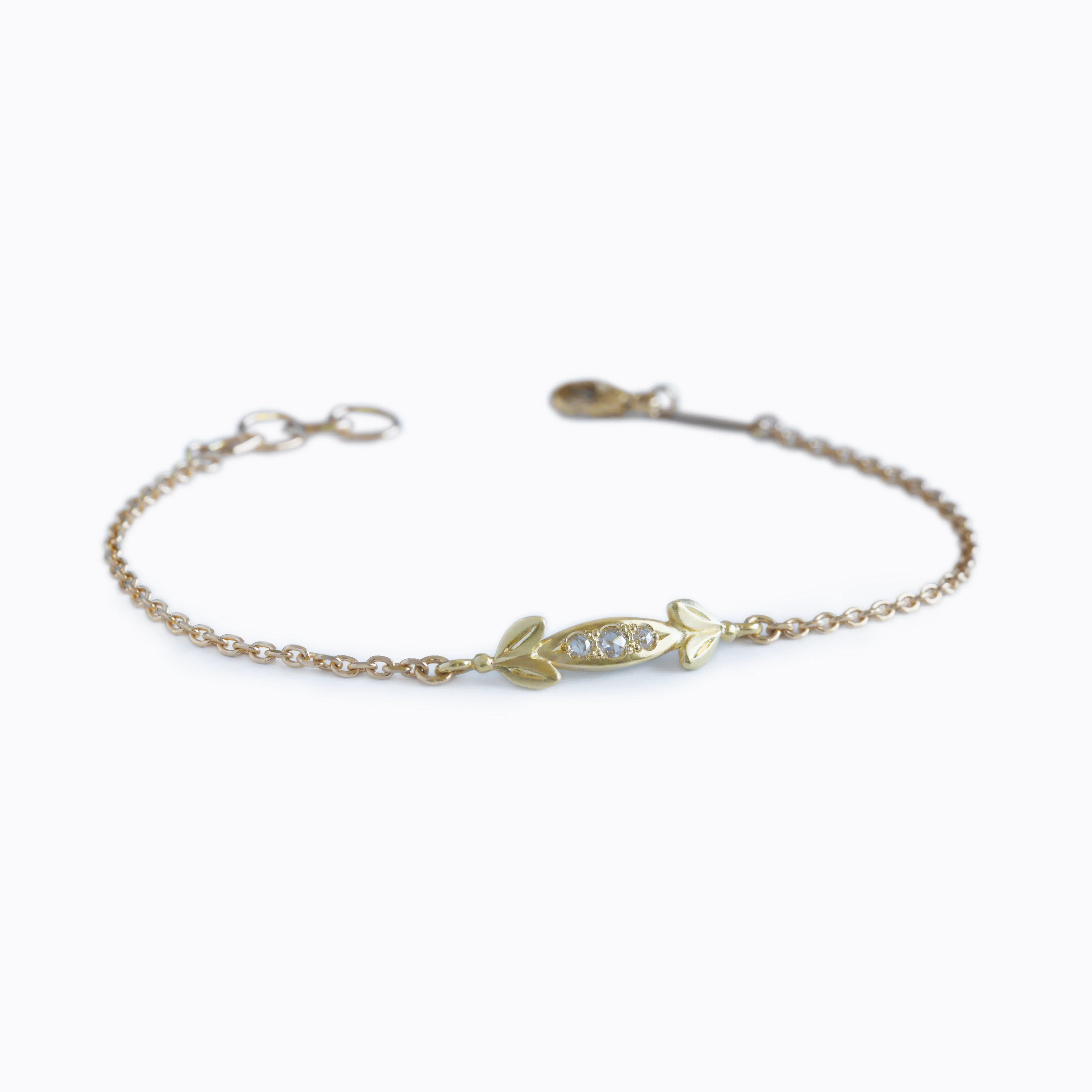 Delicate gold bracelet with small leaf motifs and central diamond cluster, soft natural lighting