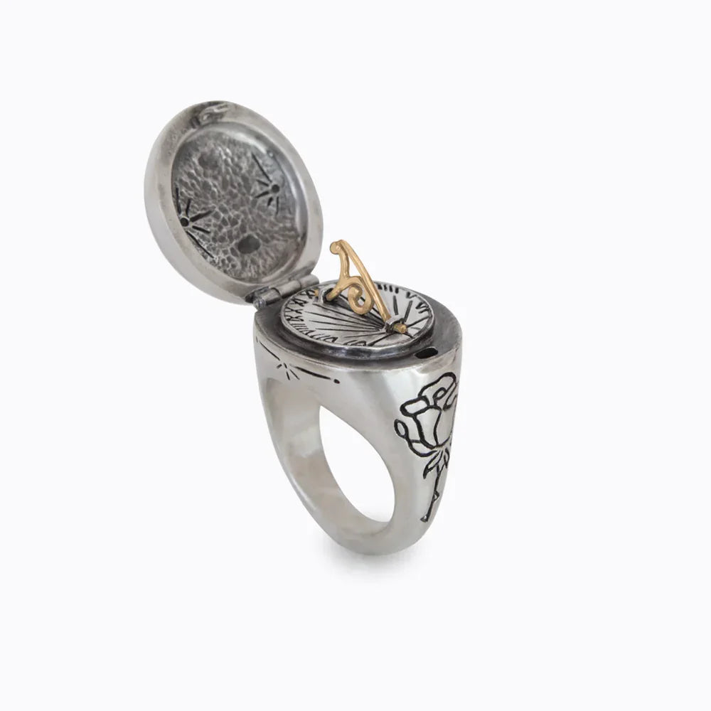 Silver sundial ring with open lid, gold gnomon, engraved rose, and hand-etched details on white background