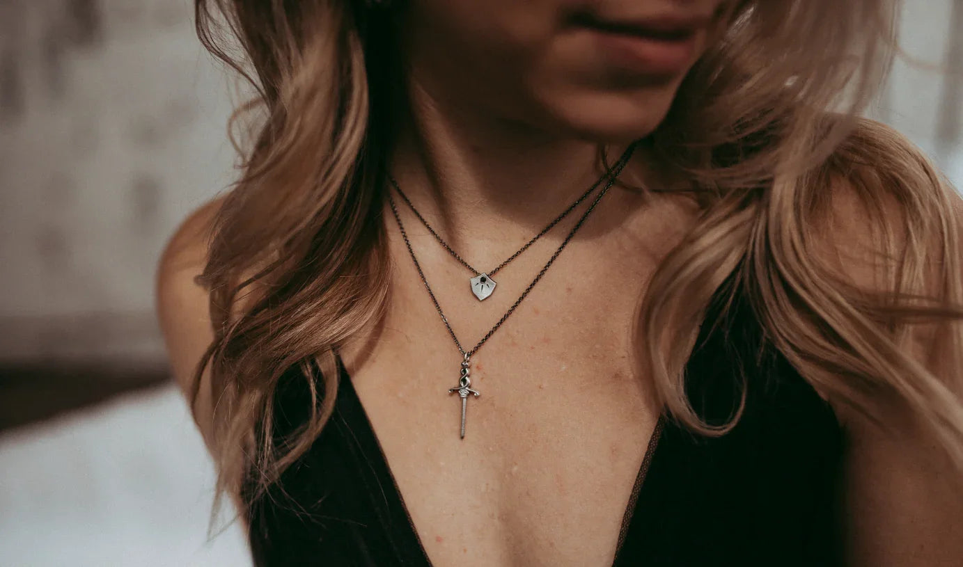 Close-up of layered sword and shield pendants on delicate gold necklaces, warm natural light