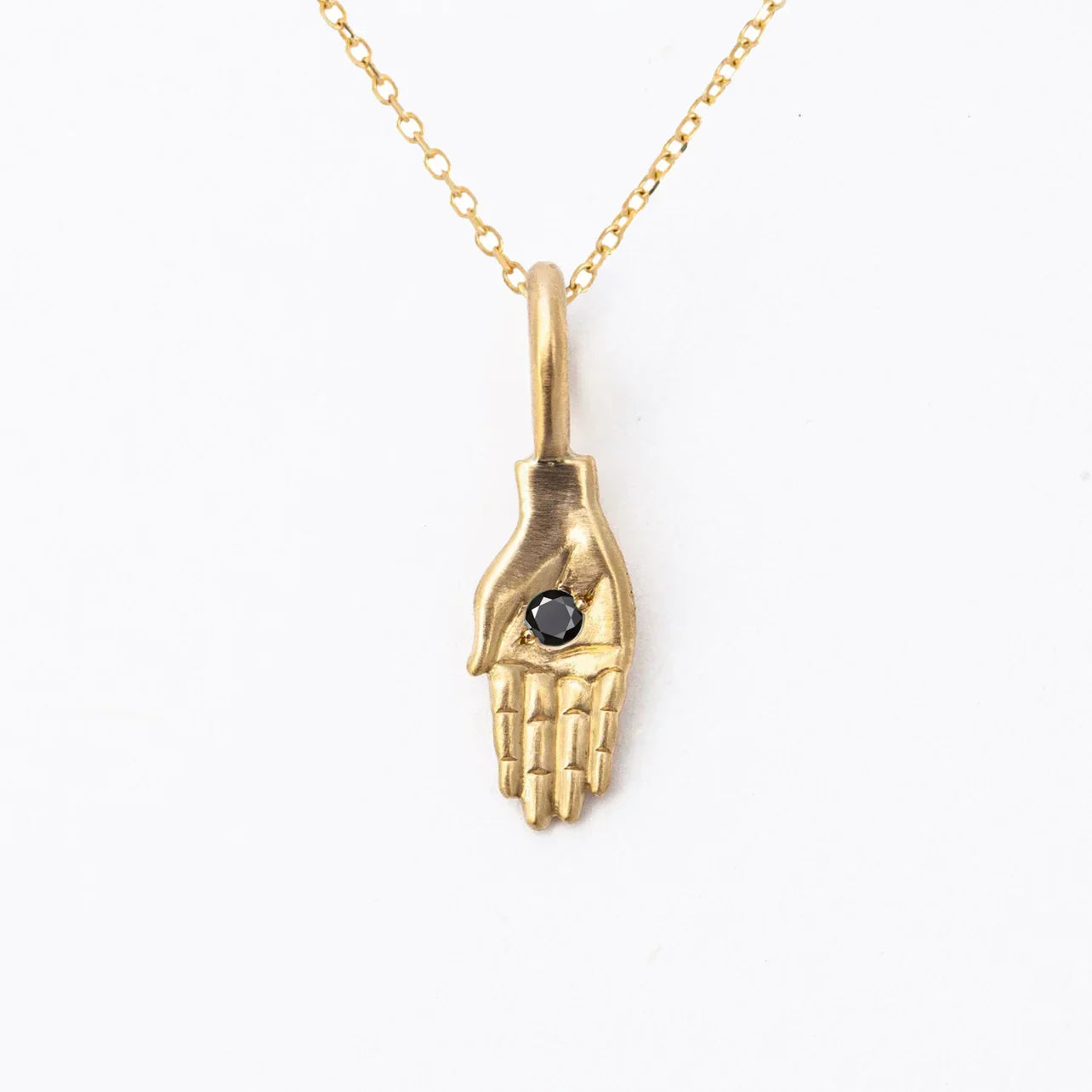 Handcrafted gold pendant shaped like a hand holding a black gemstone on delicate gold chain against white background