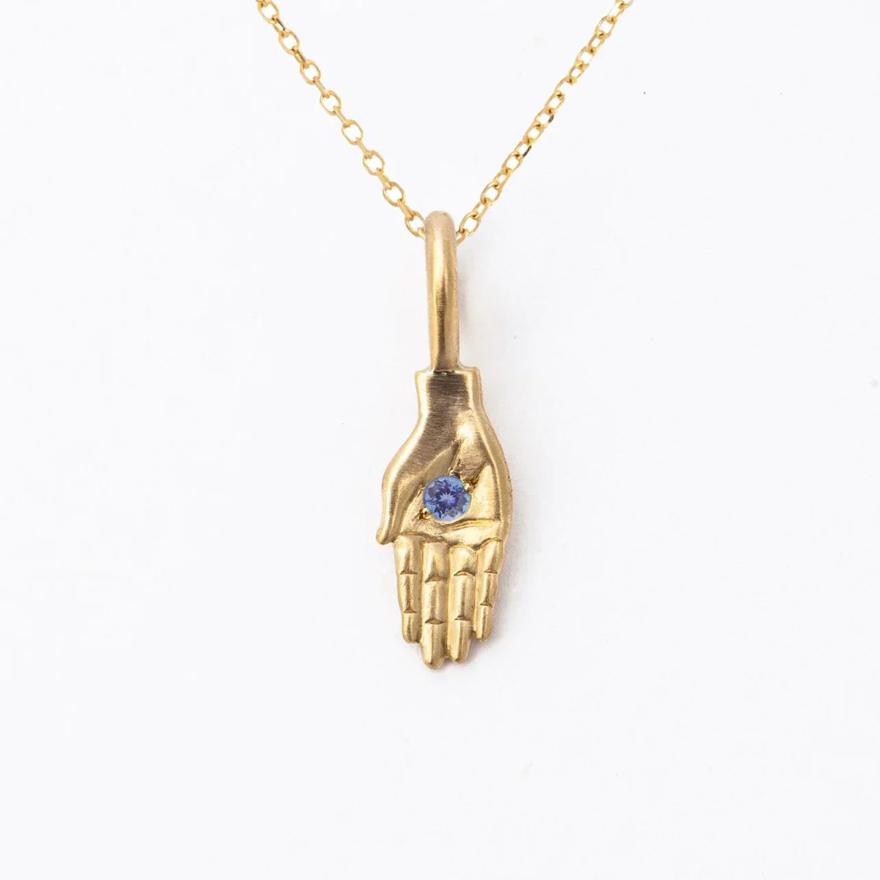 Handcrafted gold hand pendant with blue gemstone on fine gold chain, minimalist white background