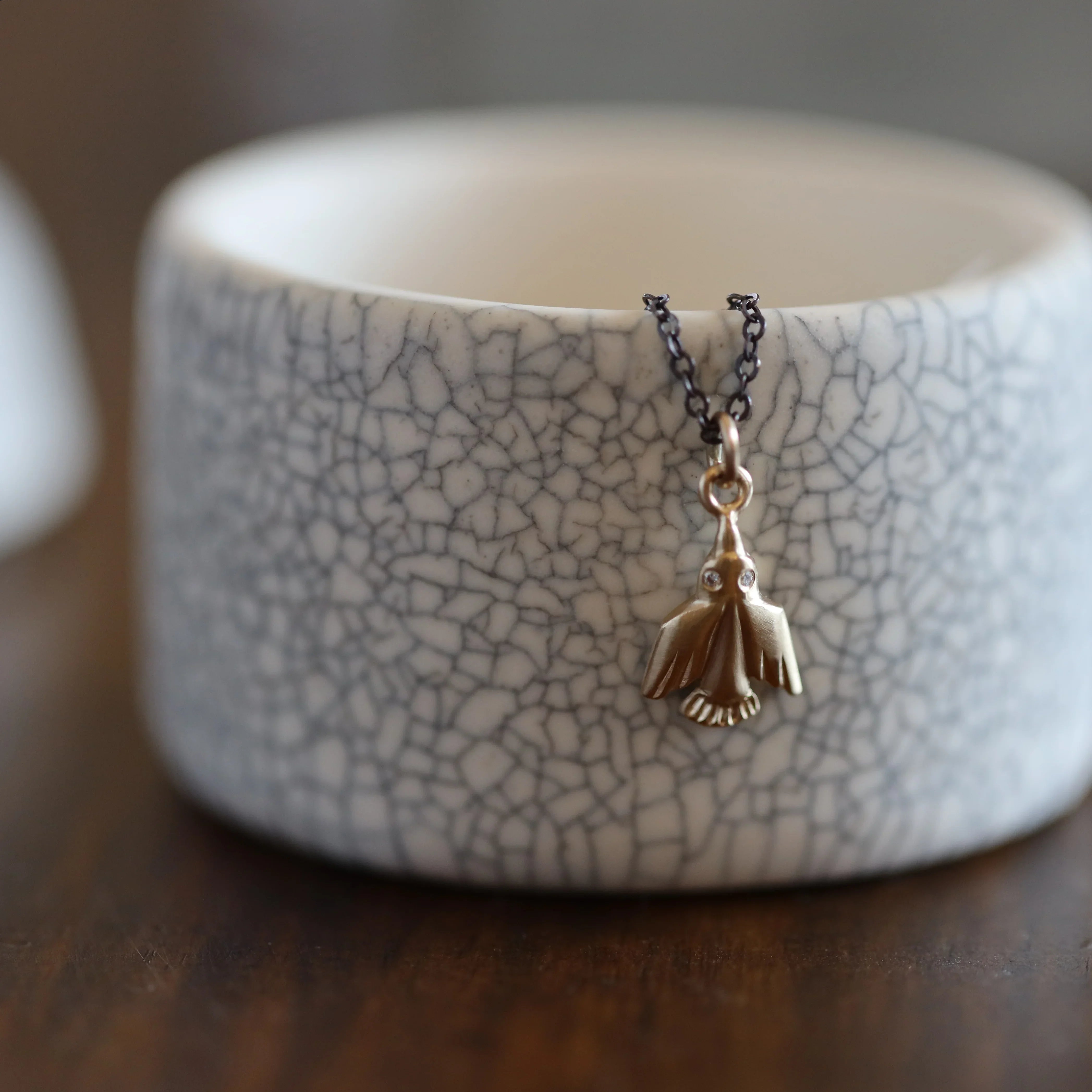 Close-up of elegant gold eagle pendant necklace with diamonds on textured ceramic, warm natural light