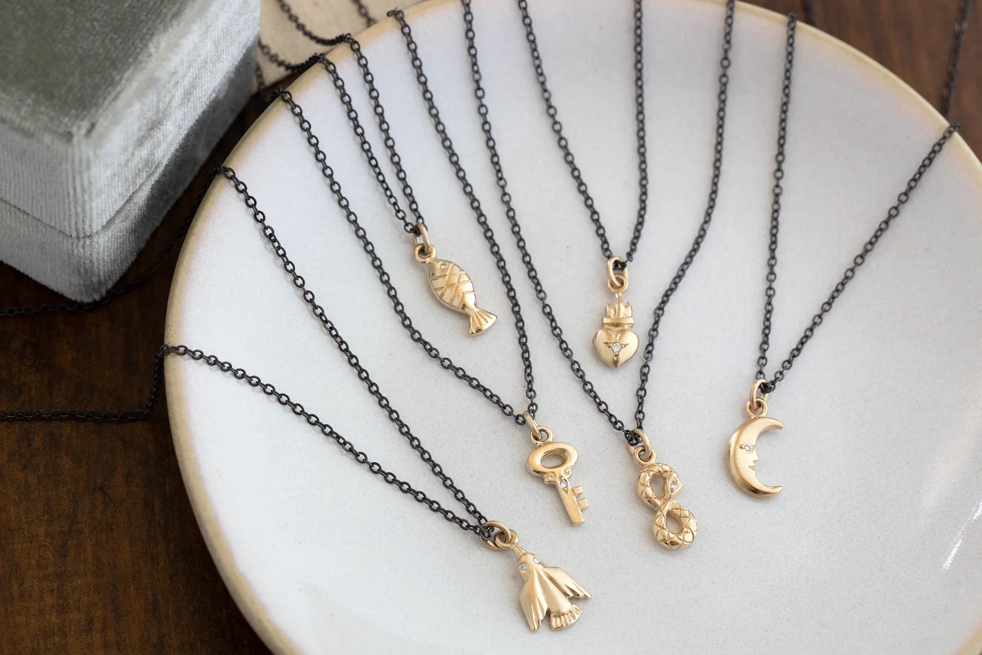 Collection of handcrafted gold charm necklaces with black chains on white ceramic plate, natural light