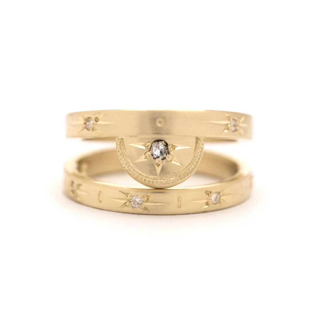 Close-up of three handcrafted Fairmined gold rings with hand-engraved star motifs and rustic diamonds on white background